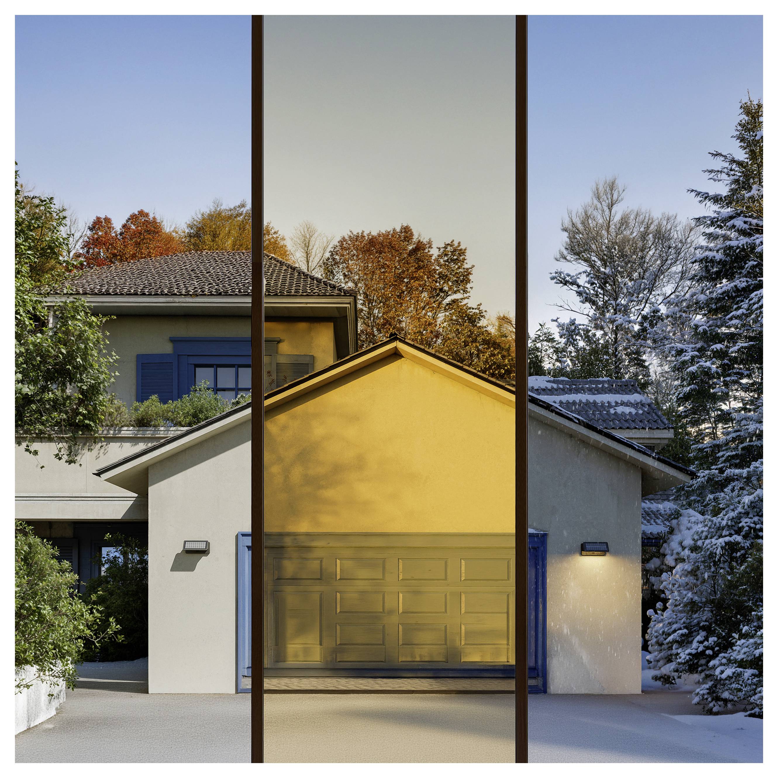 Facciata di una casa moderna vista attraverso tre vetri di finestre verticali e alte, con un garage illuminato dal sole e alberi autunnali all'esterno.