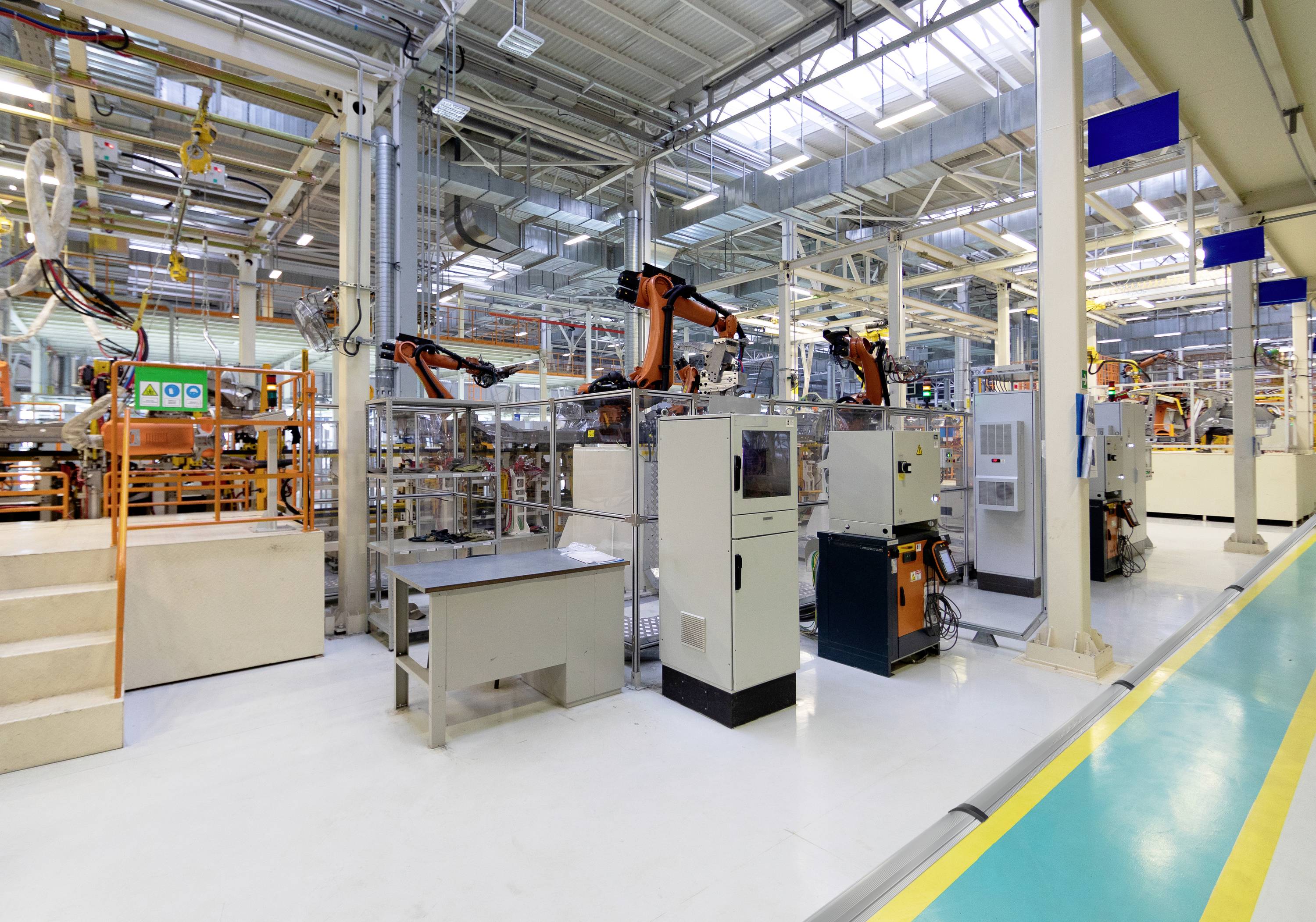 Impianto industriale di produzione con più robot in funzione. Ambiente altamente illuminato con numerose macchine e sistemi di controllo.