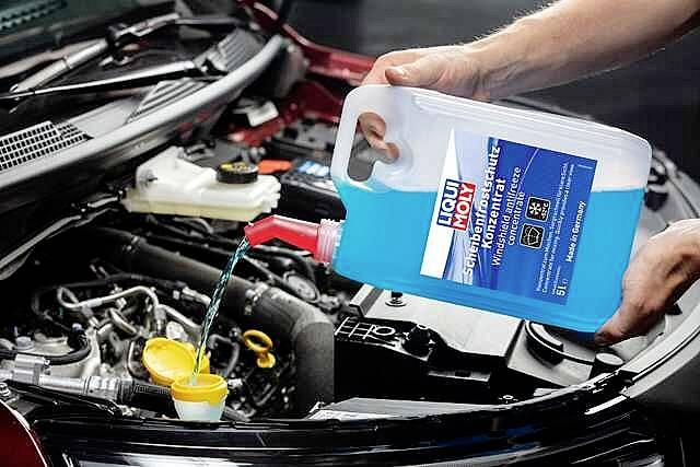 Una persona versa il liquido antigelo dal tanico nel serbatoio dei liquidi di un'auto. Il cofano è aperto.