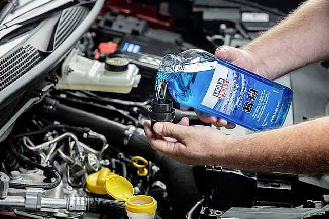 Una persona versa liquido lavavetri blu da una bottiglia nel serbatoio nel vano motore di un'auto.
