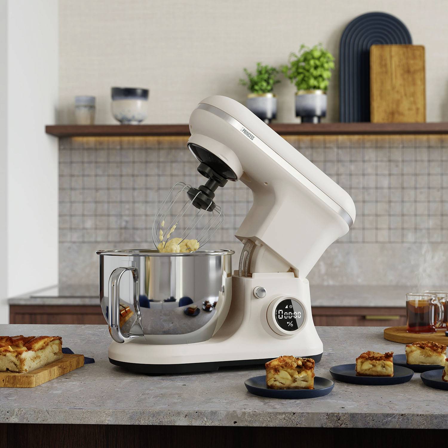 Un robot da cucina su un bancone con una frusta; sullo sfondo si vedono fette di torta e utensili da cucina.