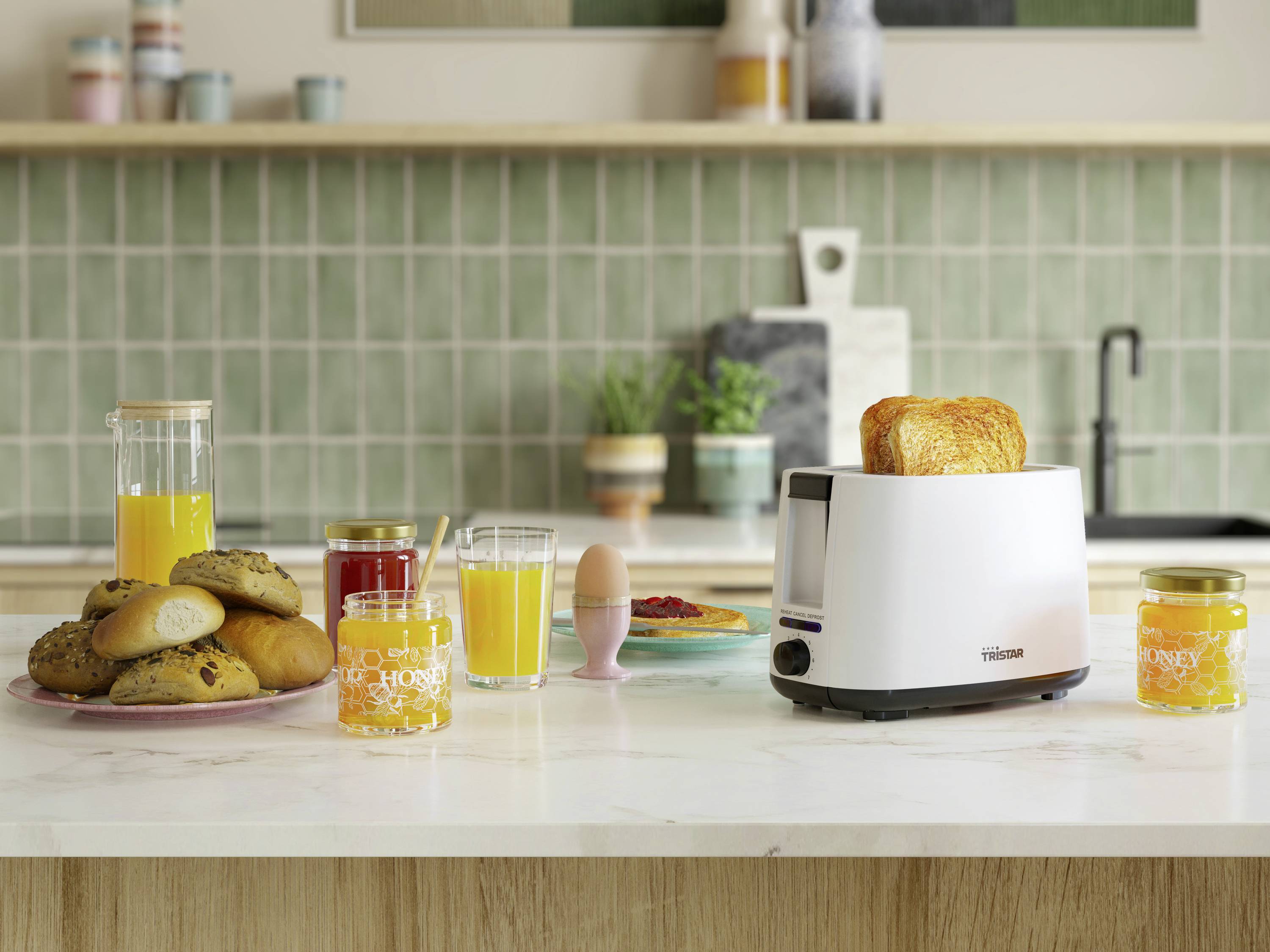 Un tavolo da colazione con toast nel tostapane, panini su un piatto, vari succhi e vasetti di marmellata davanti a una parete di piastrelle verdi.