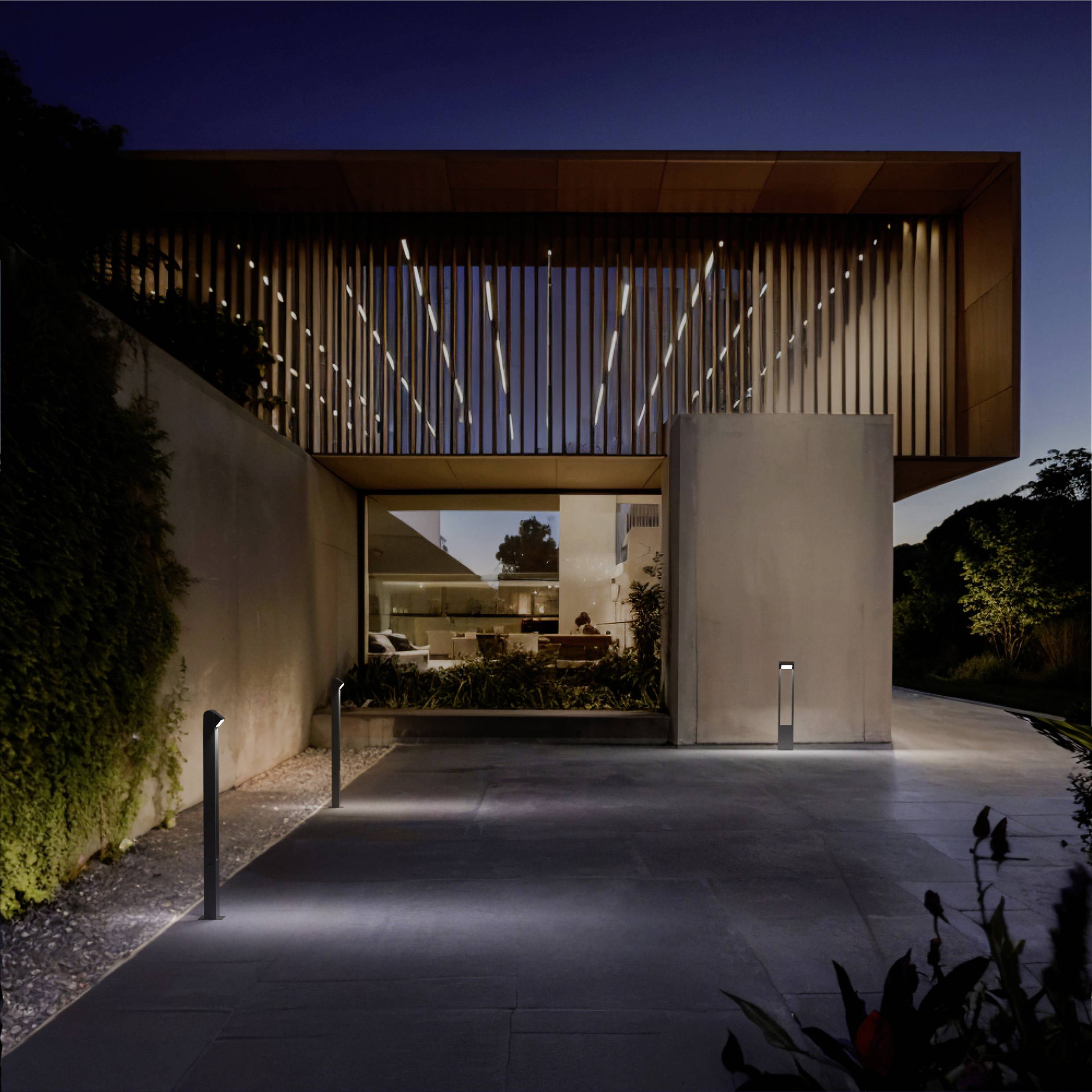 Una casa moderna al crepuscolo con design in legno a listelli e illuminazione calda, circondata da vegetazione. Architettura minimalista con grandi finestre.