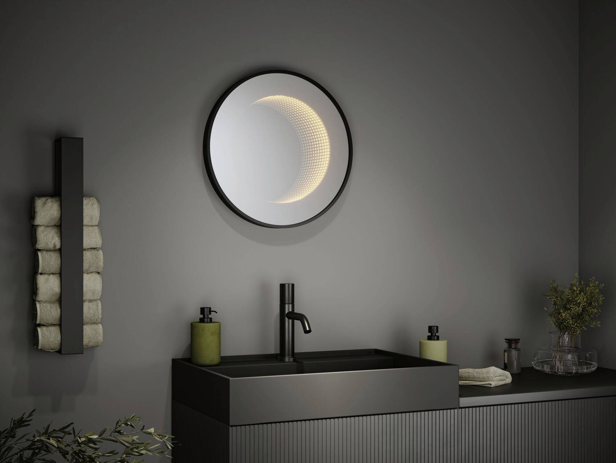 Un bagno con un lavabo scuro, un rubinetto stilizzato, uno specchio rotondo che mostra un design a mezzaluna luminoso e degli asciugamani.