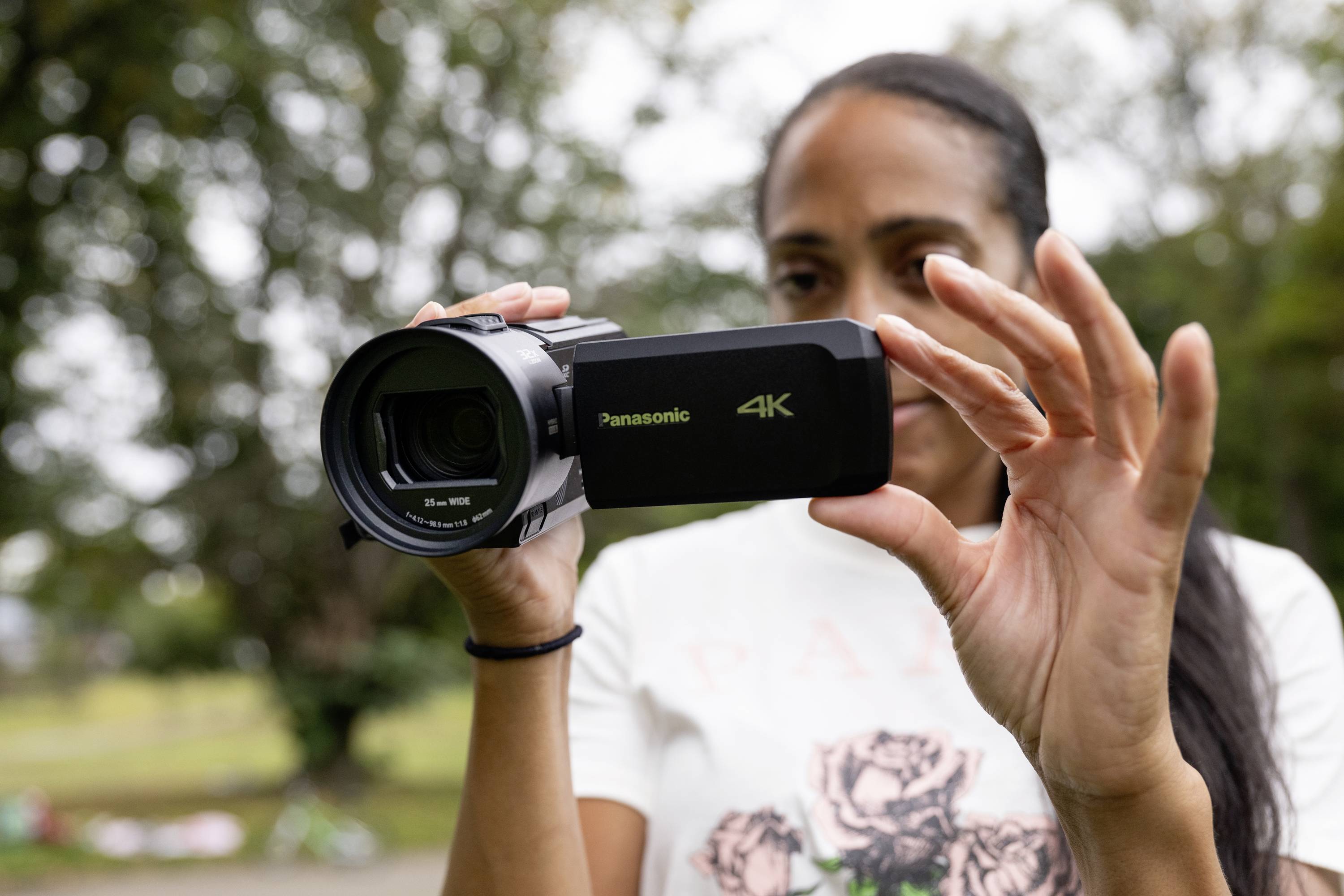 Una persona sta tenendo una videocamera 4K all'aperto. La scena sembra essere in un parco, circondato da alberi sullo sfondo.
