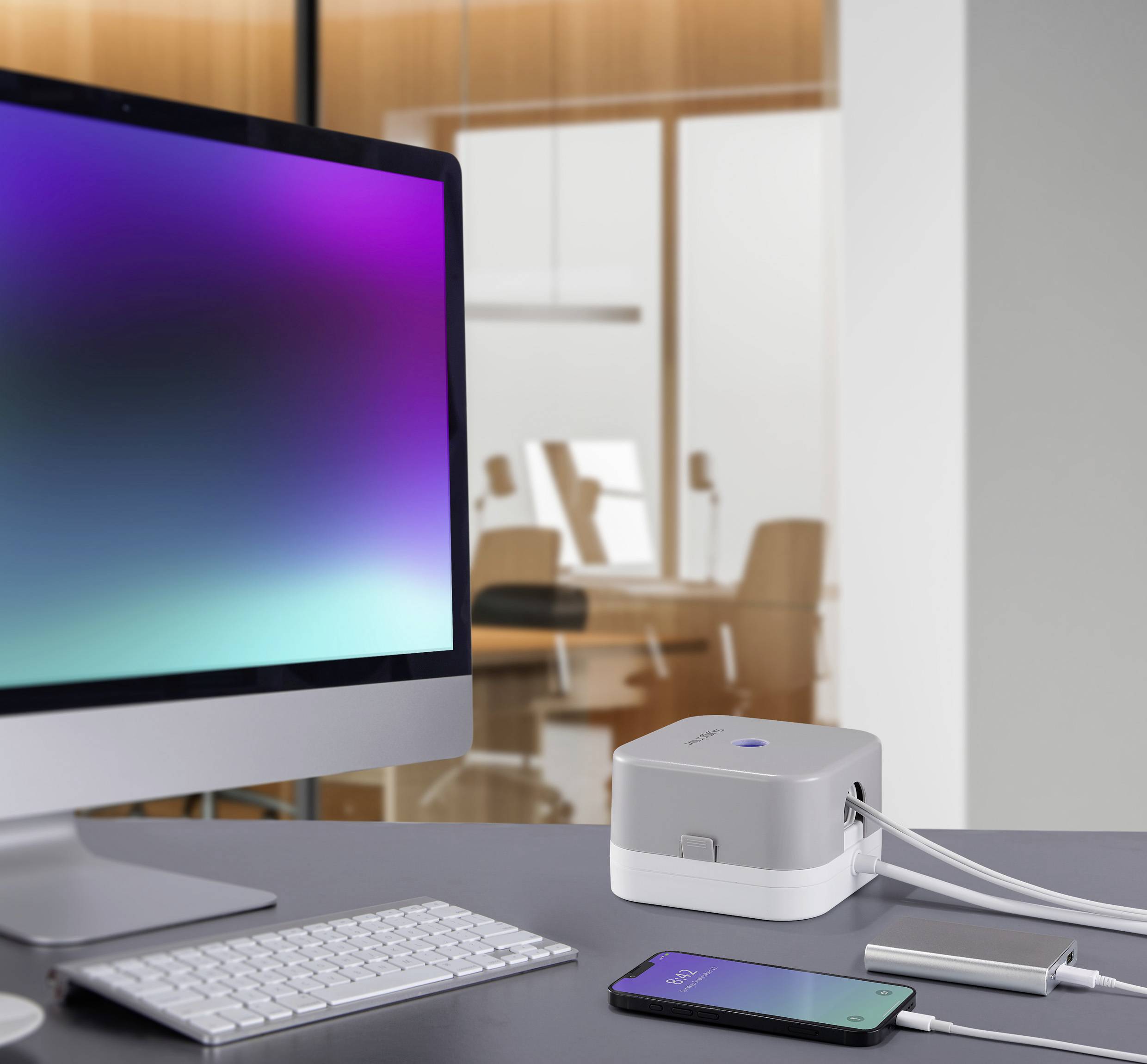 Un monitor, uno smartphone e un dispositivo cubico su una scrivania in un ufficio moderno. Il dispositivo sembra fungere da caricabatterie.