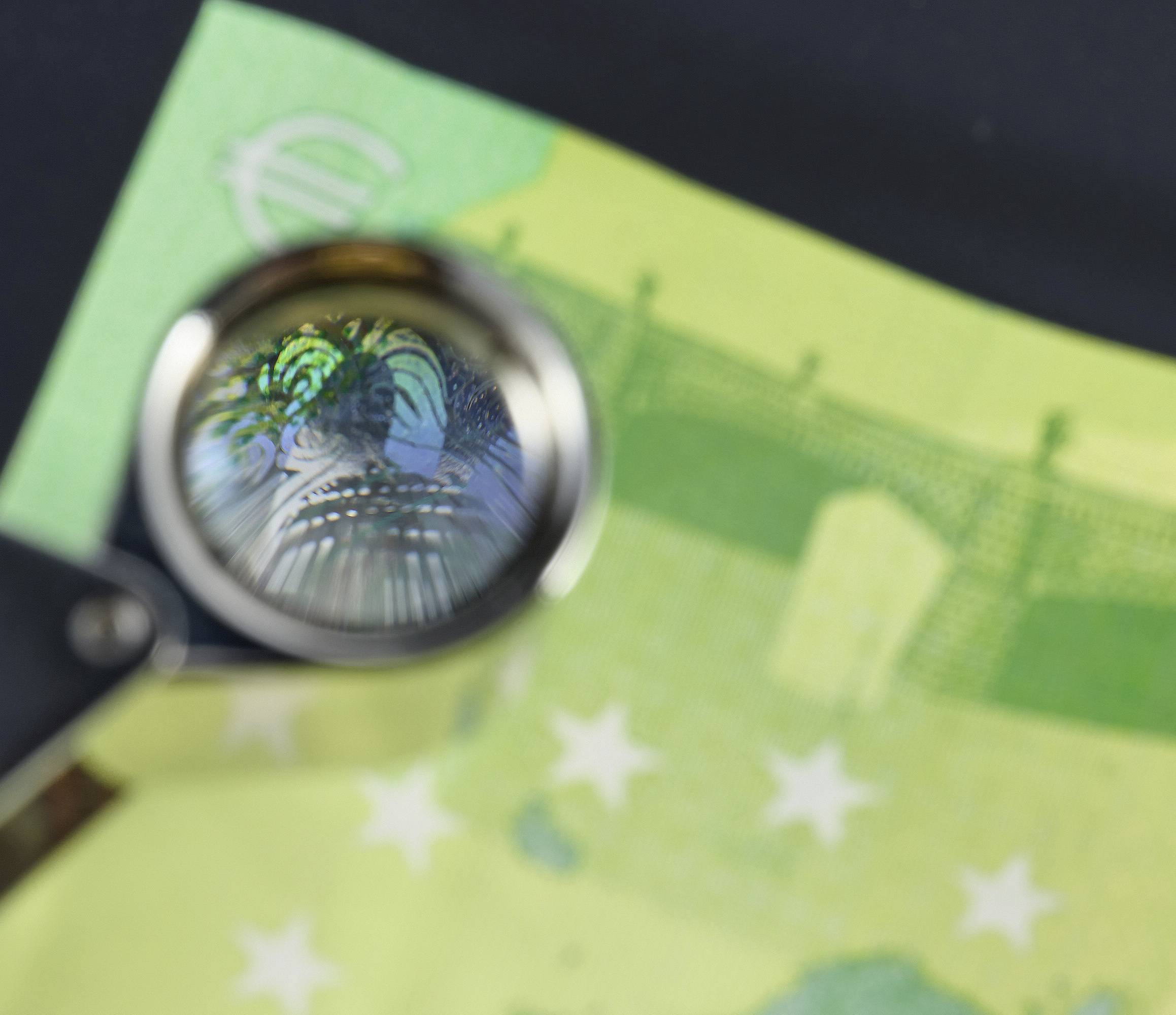 Una lente di ingrandimento evidenzia le caratteristiche di sicurezza su un banconota in euro, concentrandosi sugli ologrammi e sui dettagli intricati della valuta.