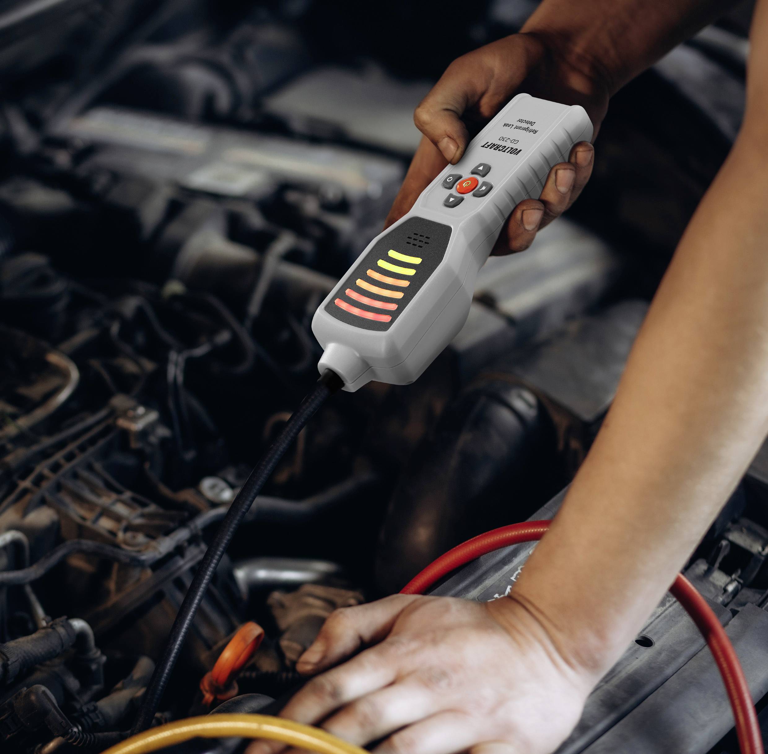 Una persona che utilizza un dispositivo diagnostico palmare su un motore di un'automobile, controllando eventuali problemi. Il dispositivo ha indicatori luminosi che mostrano i risultati.