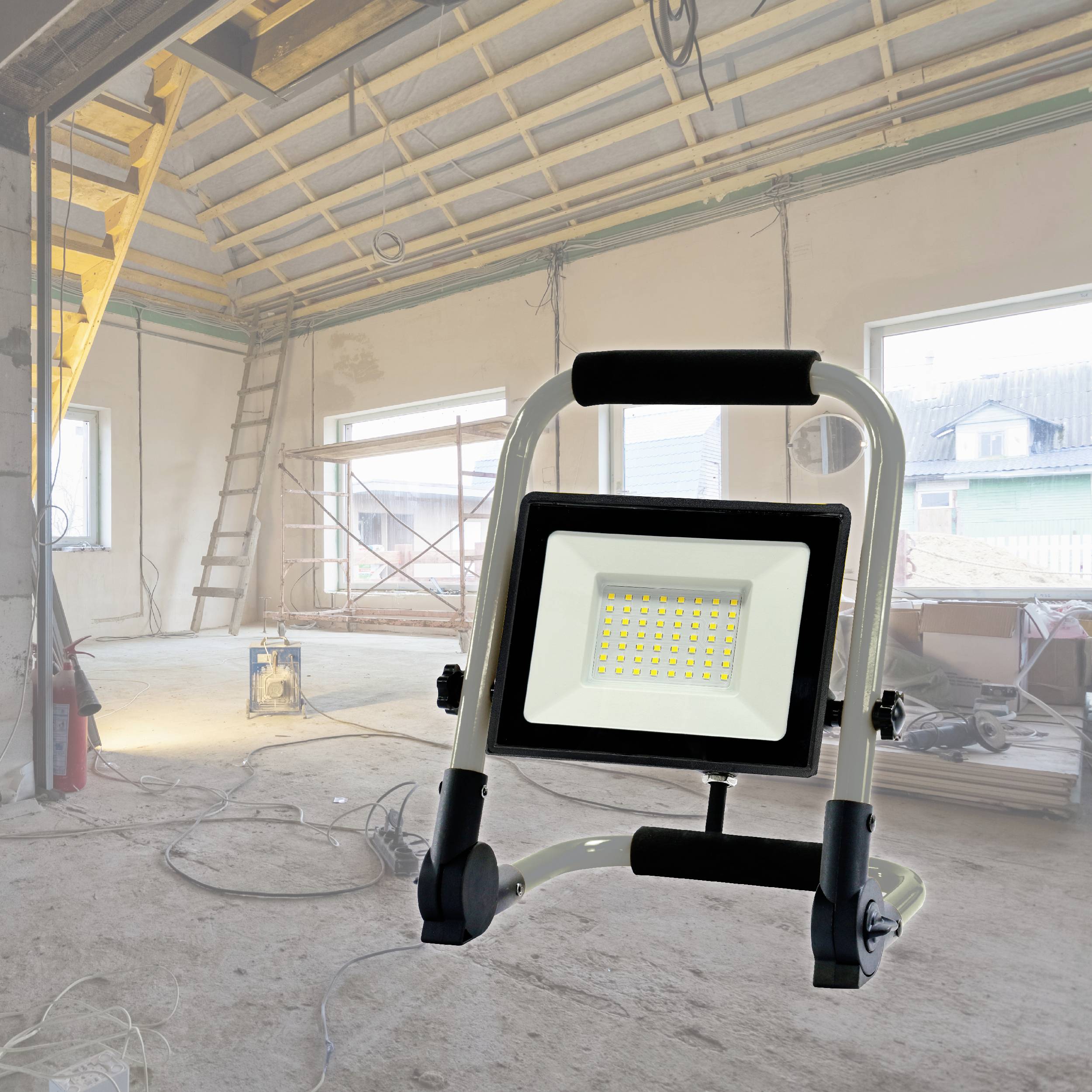 Un progetto di costruzione in un edificio grezzo con una scala, cavi e un faro da cantiere in primo piano. La luce diurna illumina l'ambiente.