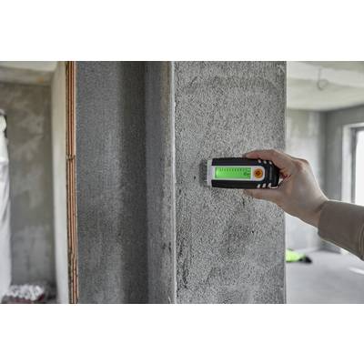 Una persona misura l'umidità in un muro di cemento utilizzando un misuratore di umidità digitale. Il display mostra il valore misurato.