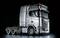 Un camion argento con quattro assi su sfondo nero. Sulla cabina di guida è scritto 'SCANIA'.