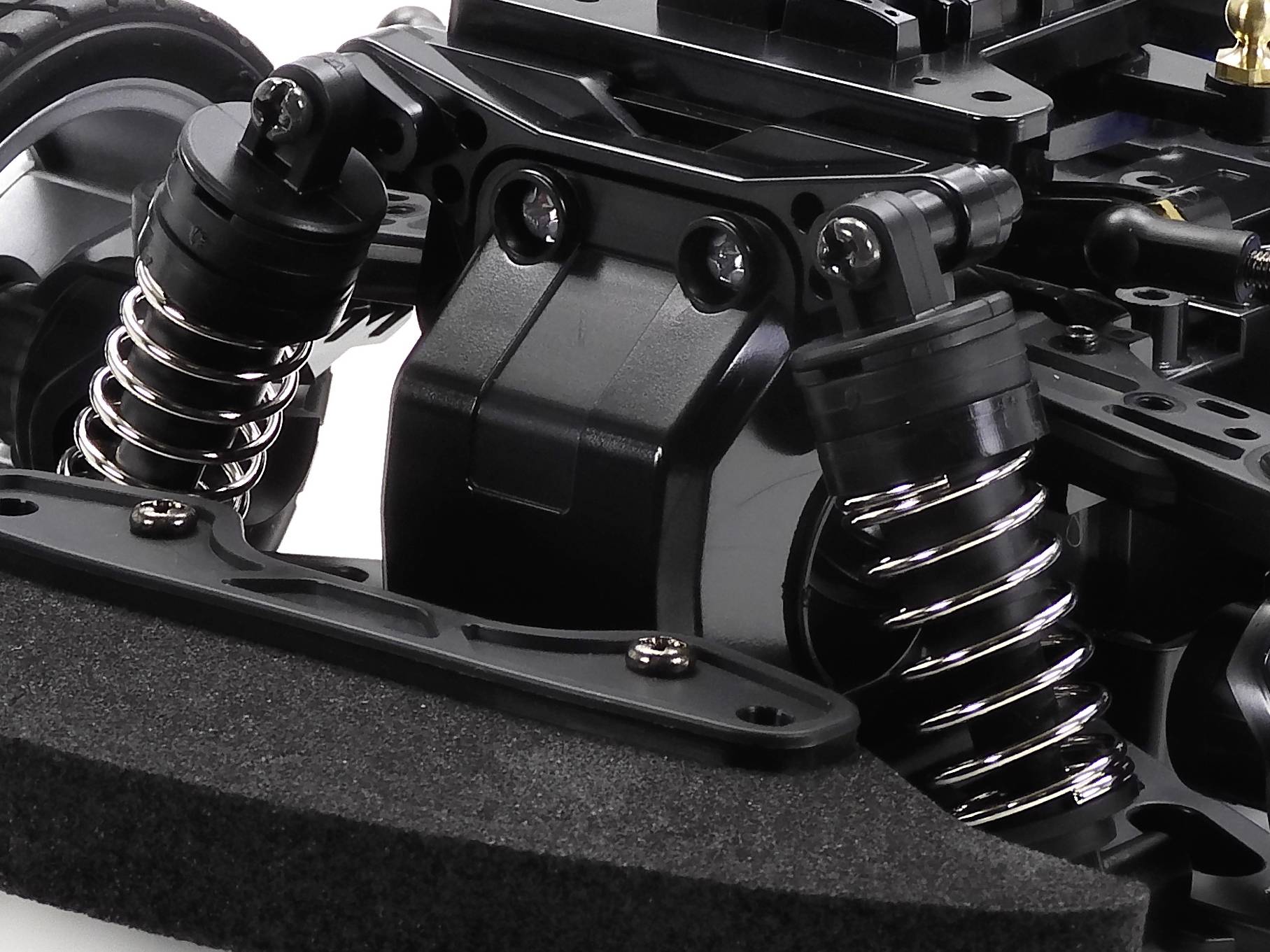 Primo piano del telaio di un'auto radiocomandata verniciata di nero, con ammortizzatori e sospensioni, concentrato sui componenti anteriori.