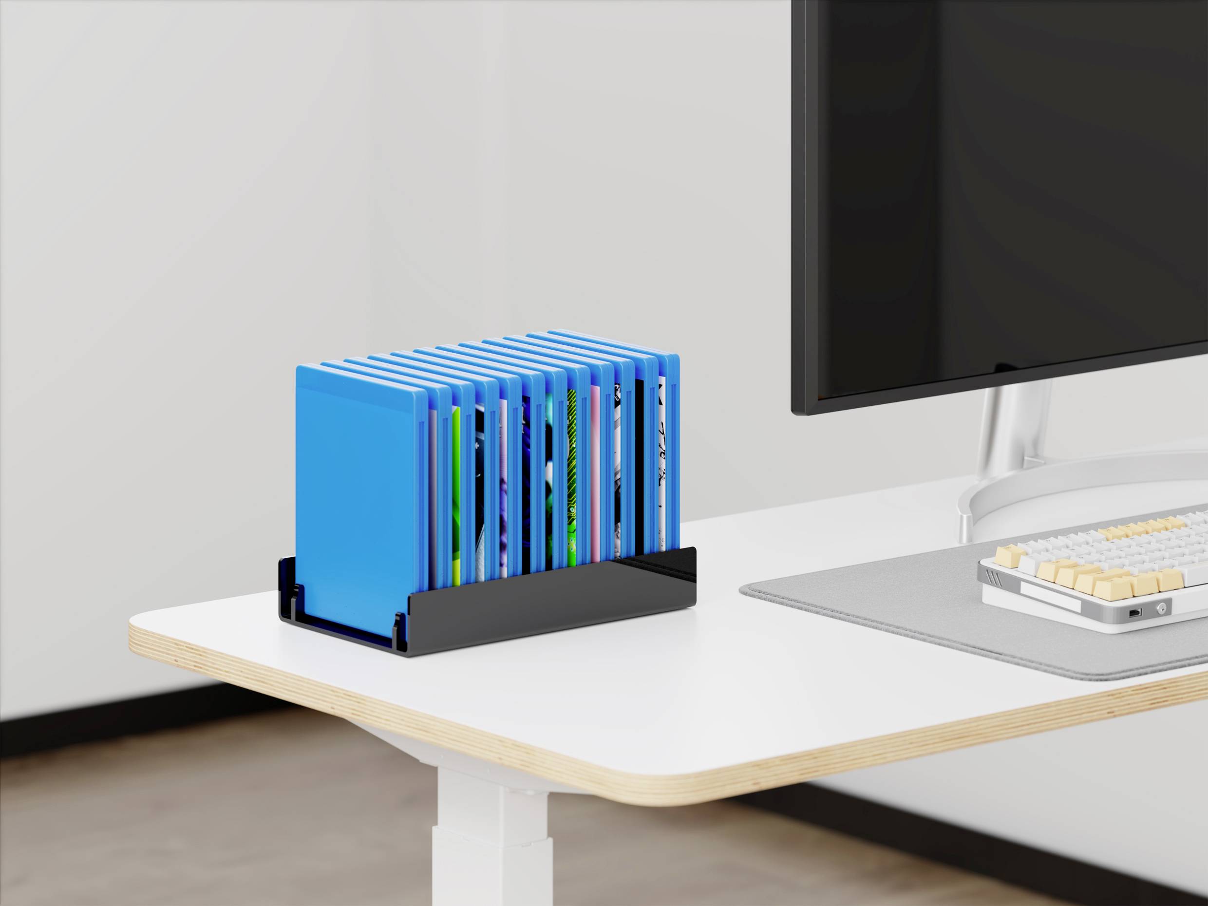 Cartelle blu in un organizzatore nero su una scrivania bianca accanto a un monitor del computer.