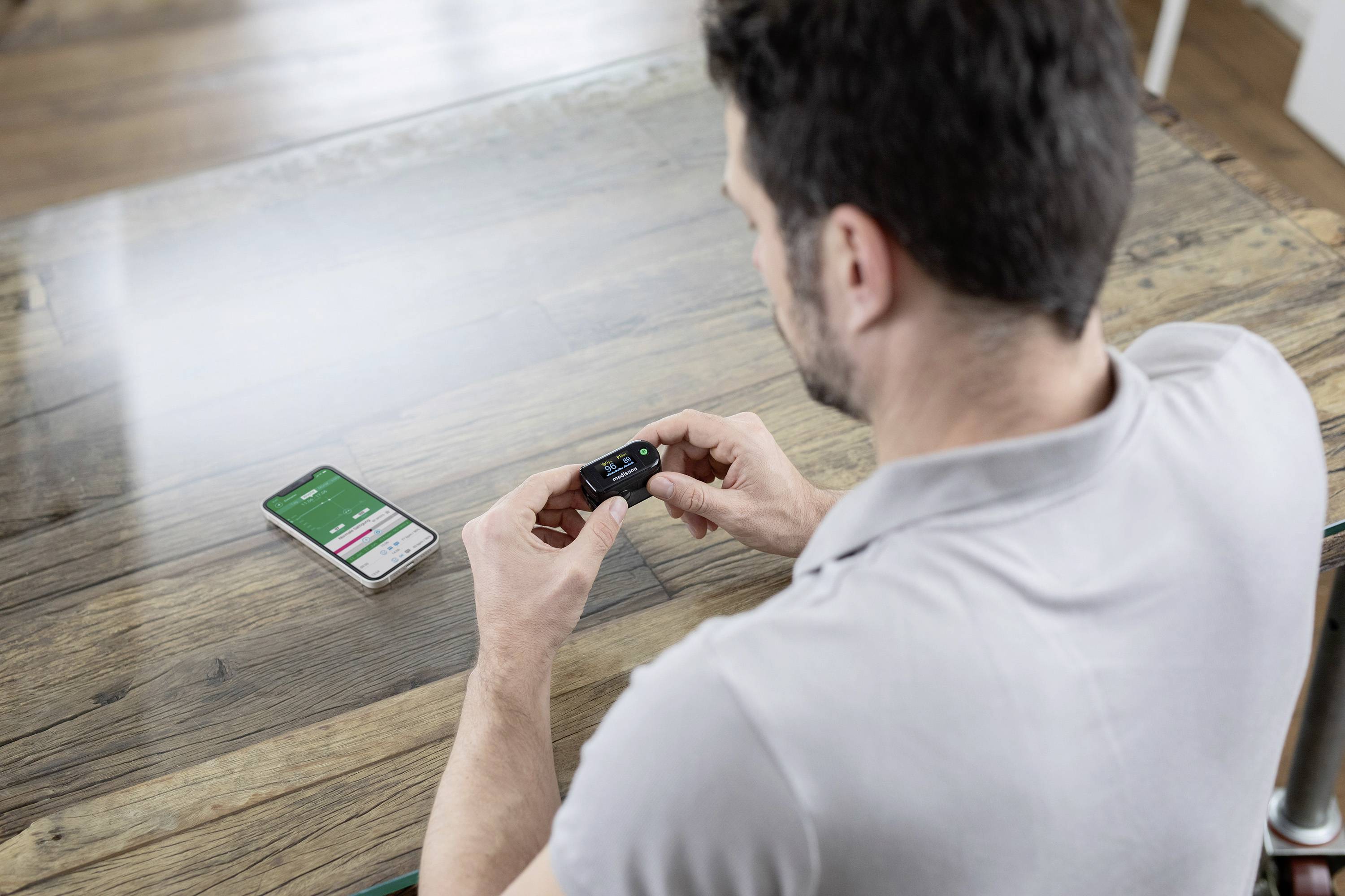 Un uomo sta utilizzando un dispositivo fitness tracker. Sul tavolo c'è uno smartphone con un'app per la salute aperta.