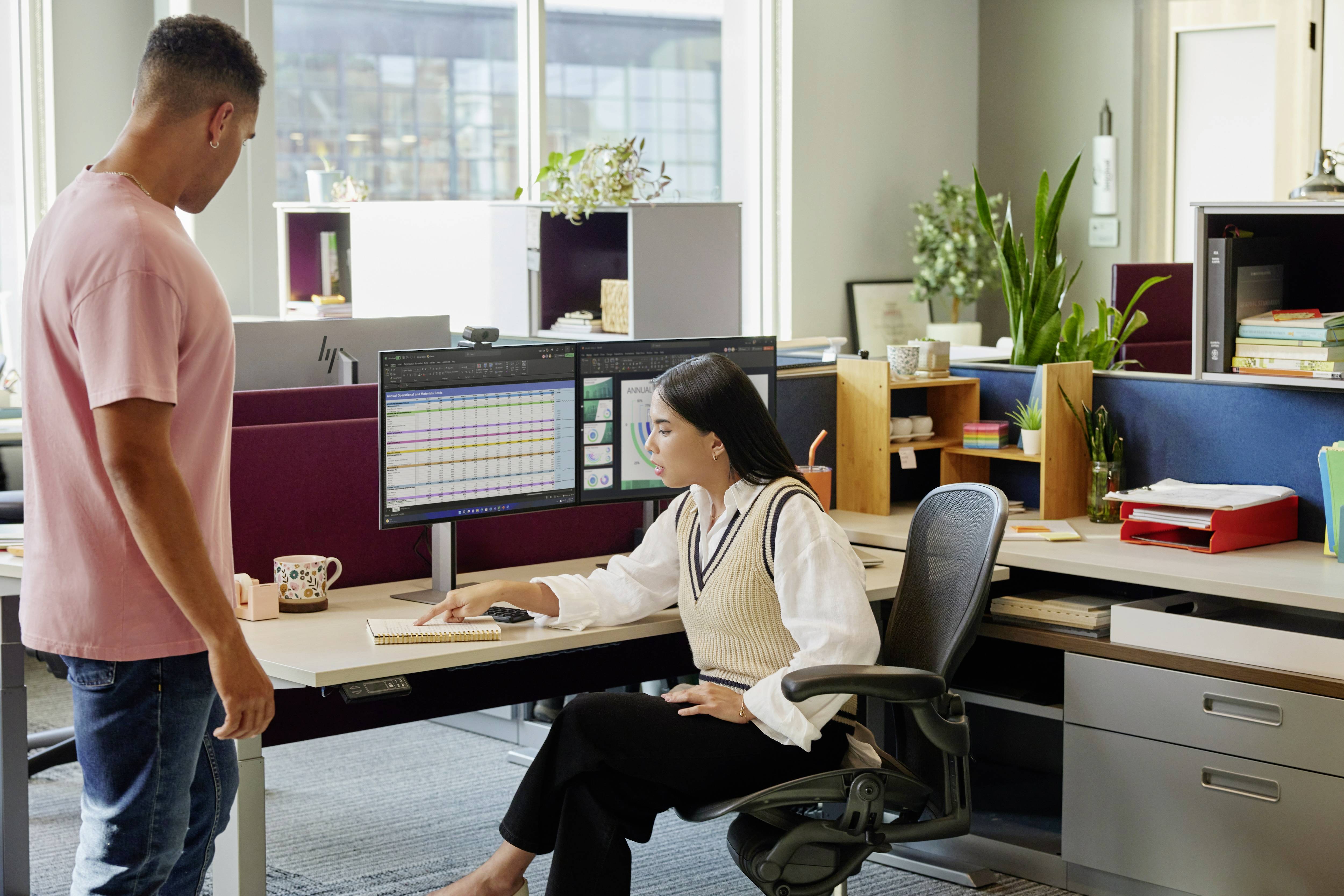 Un uomo e una donna in un ufficio moderno, che guardano insieme grandi monitor con diagrammi e dati. La donna è seduta davanti al computer.