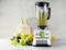 Frullatore con contenitore pieno, circondato da lime, arance e kiwi. Due bicchieri di smoothie e fresche foglie di menta in primo piano.