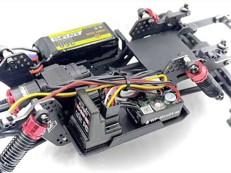 Primo piano del telaio di un'auto radiocomandata con elettronica e cablaggio, inclusi batteria e ammortizzatori.