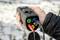 Una persona tiene un dispositivo elettrico di misurazione con cavi colorati, utilizzato per test di sicurezza e funzionalità di sistemi elettrici. Sullo sfondo neve sull'erba.