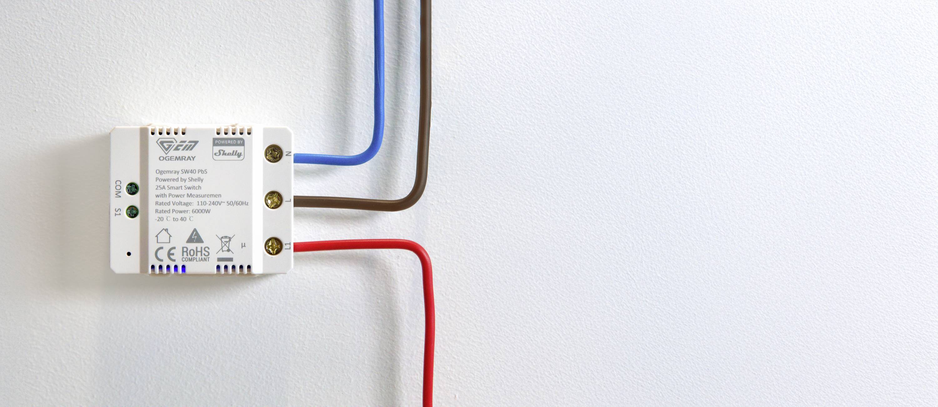 Un dispositivo elettronico con tre cavi colorati collegati (blu, marrone, rosso) è montato su una parete bianca.