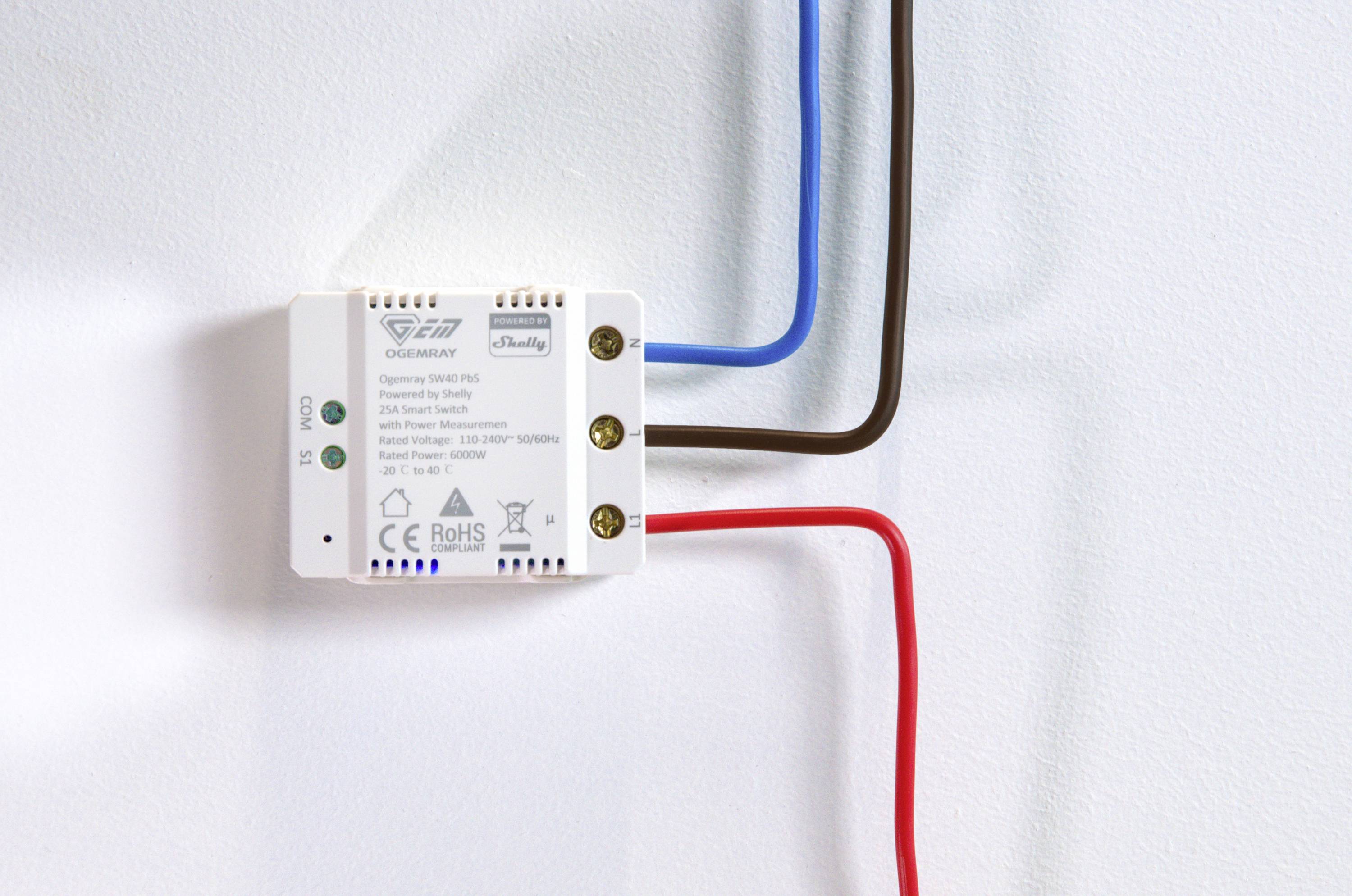 Un piccolo dispositivo elettrico con tre cavi collegati: blu, marrone e rosso. L'etichetta mostra le specifiche tecniche.
