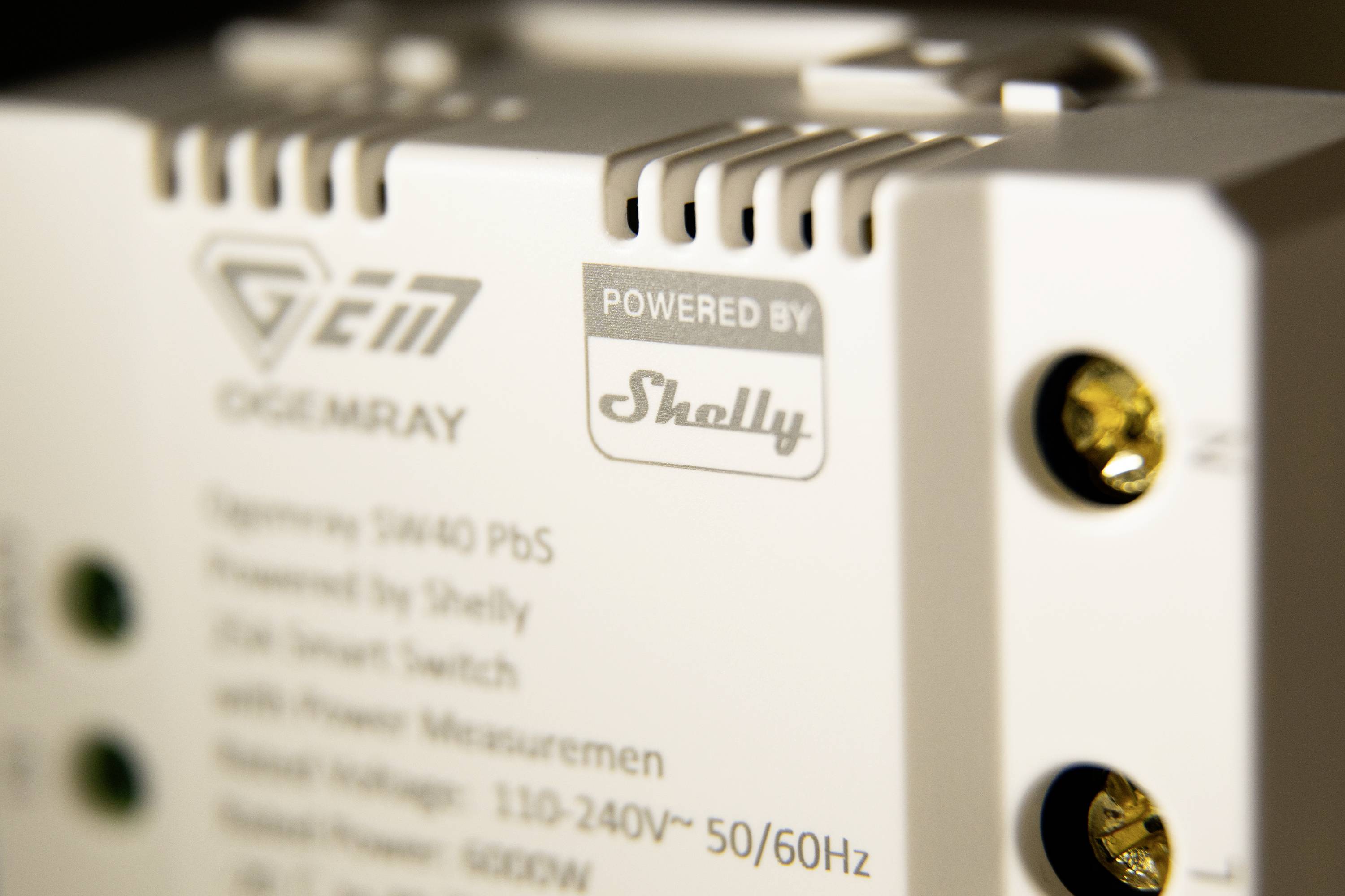 Primo piano di un dispositivo con le scritte 'Powered by Shelly' e 'GEM'. Mostra connettori e testo relativo alle specifiche di potenza.