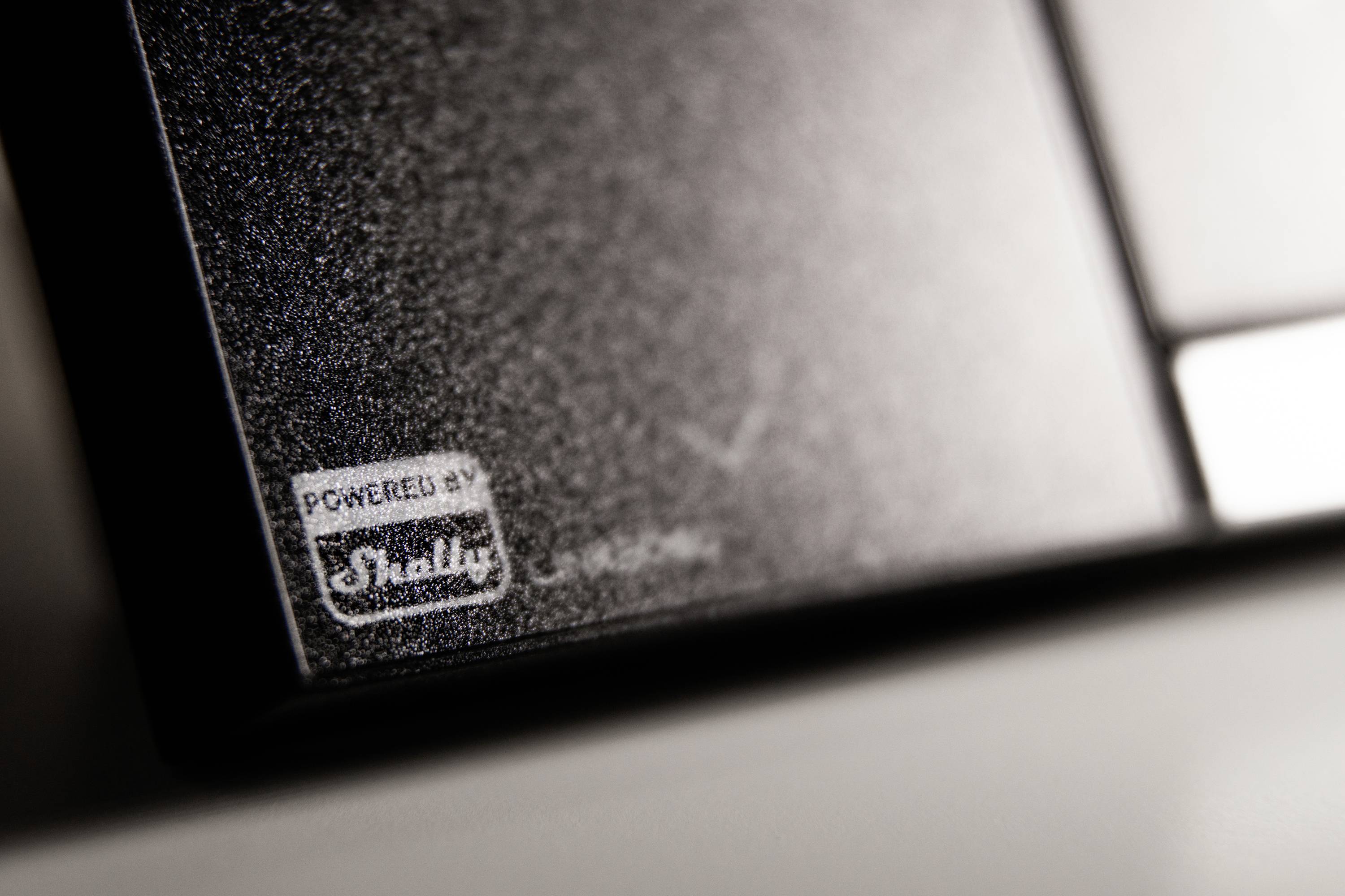 Primo piano di un dispositivo con la scritta 'Powered by Shelly'. Il logo è visibile e la superficie ha una texture strutturata.