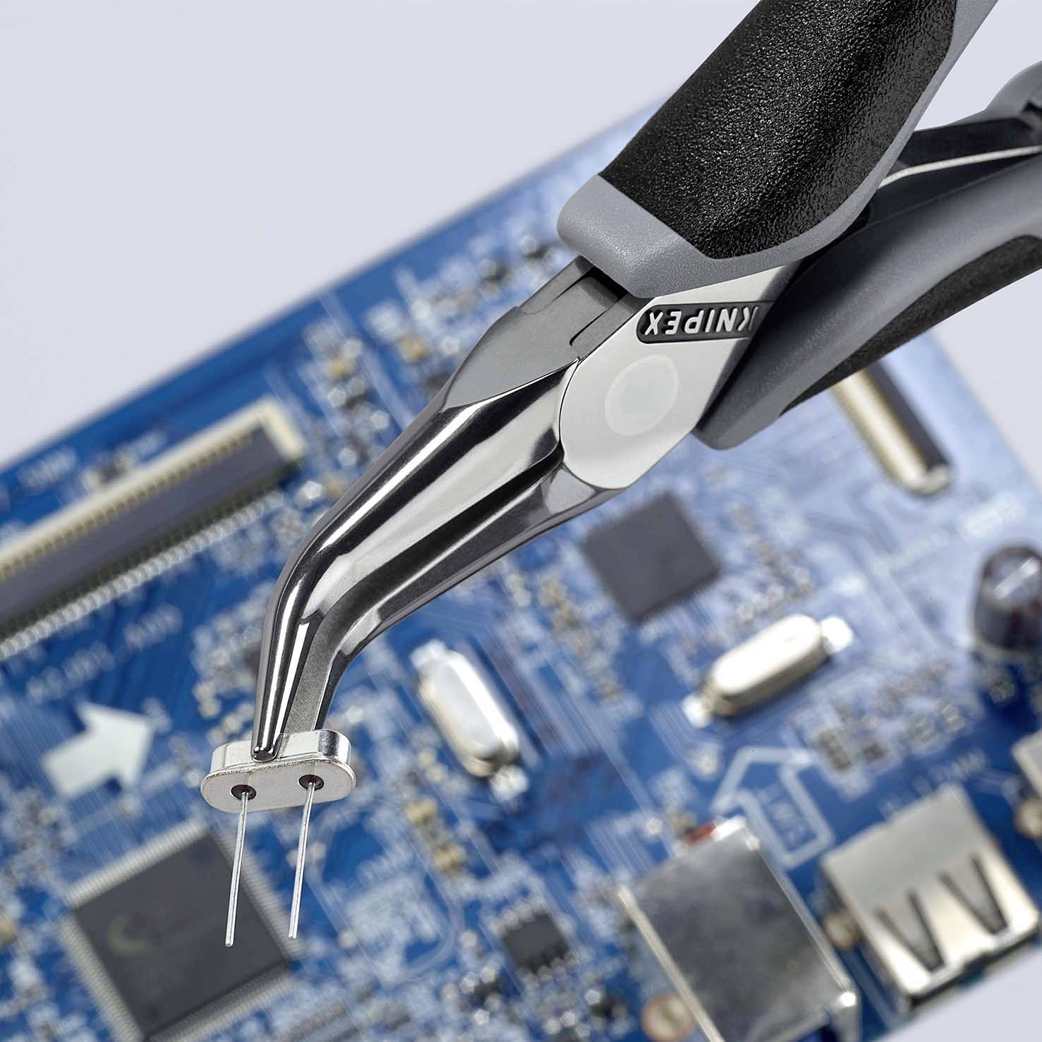 Una pinza posiziona componenti elettronici su una scheda madre del computer, dotata di vari chip e connettori.