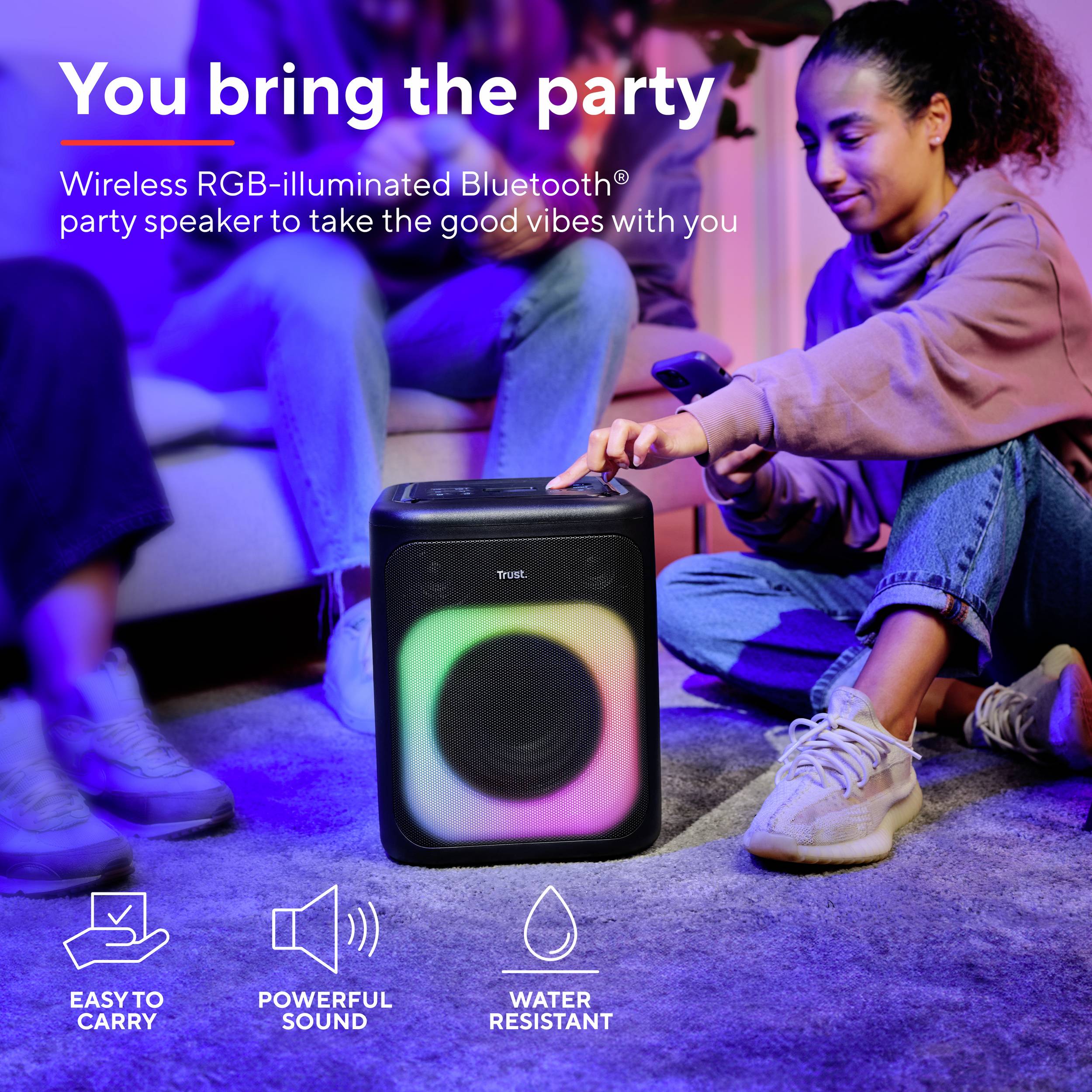 "Porti tu la festa" – Due persone sedute, ascoltano musica da un altoparlante Bluetooth portatile con illuminazione RGB nella stanza.
