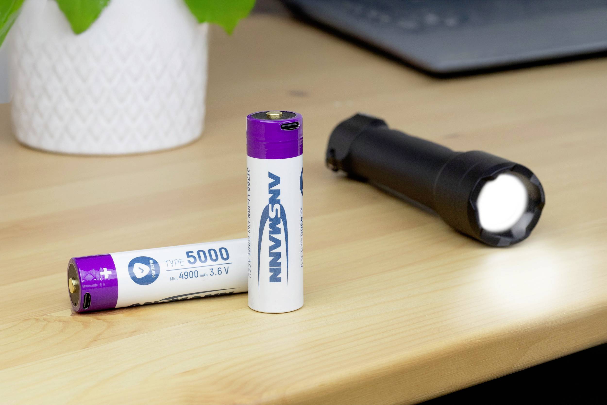 Due batterie su un tavolo, una in piedi e una sdraiata con l'etichetta 'Tipo 5000'. Sullo sfondo è visibile una torcia accesa.