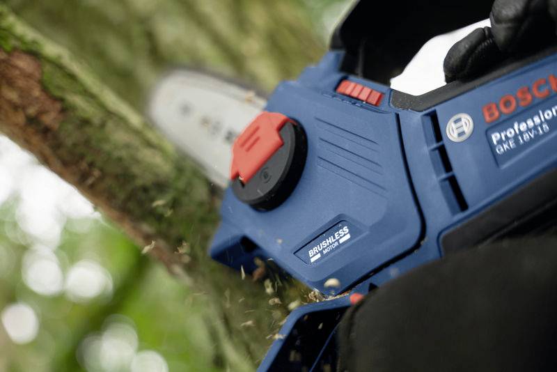 Una motosega a batteria Bosch blu taglia un ramo di un albero. Un primo piano mostra i dettagli della sega e i trucioli durante il taglio.
