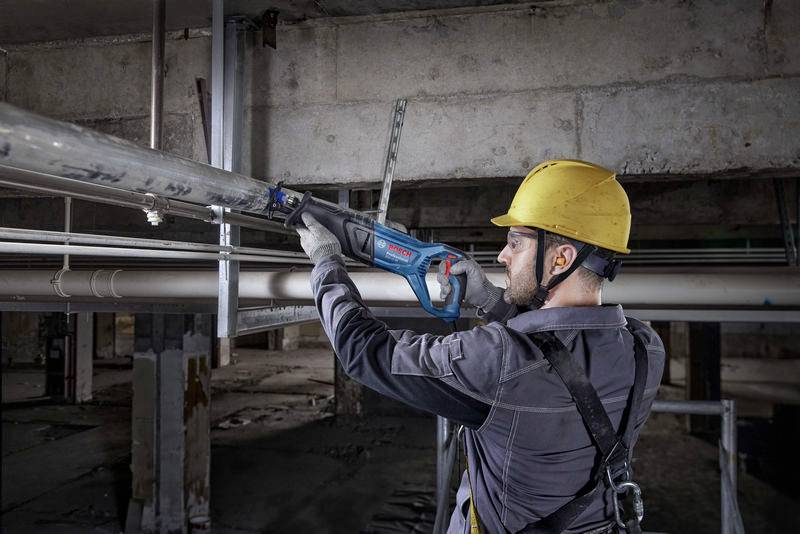 Un operaio edile con il casco di sicurezza utilizza una sega elettrica per tagliare un tubo metallico all'interno di un edificio.