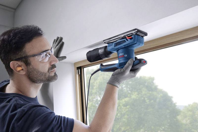 Un uomo con occhiali protettivi utilizza una smerigliatrice elettrica per lavorare un davanzale. Sullo sfondo è visibile un paesaggio verde.