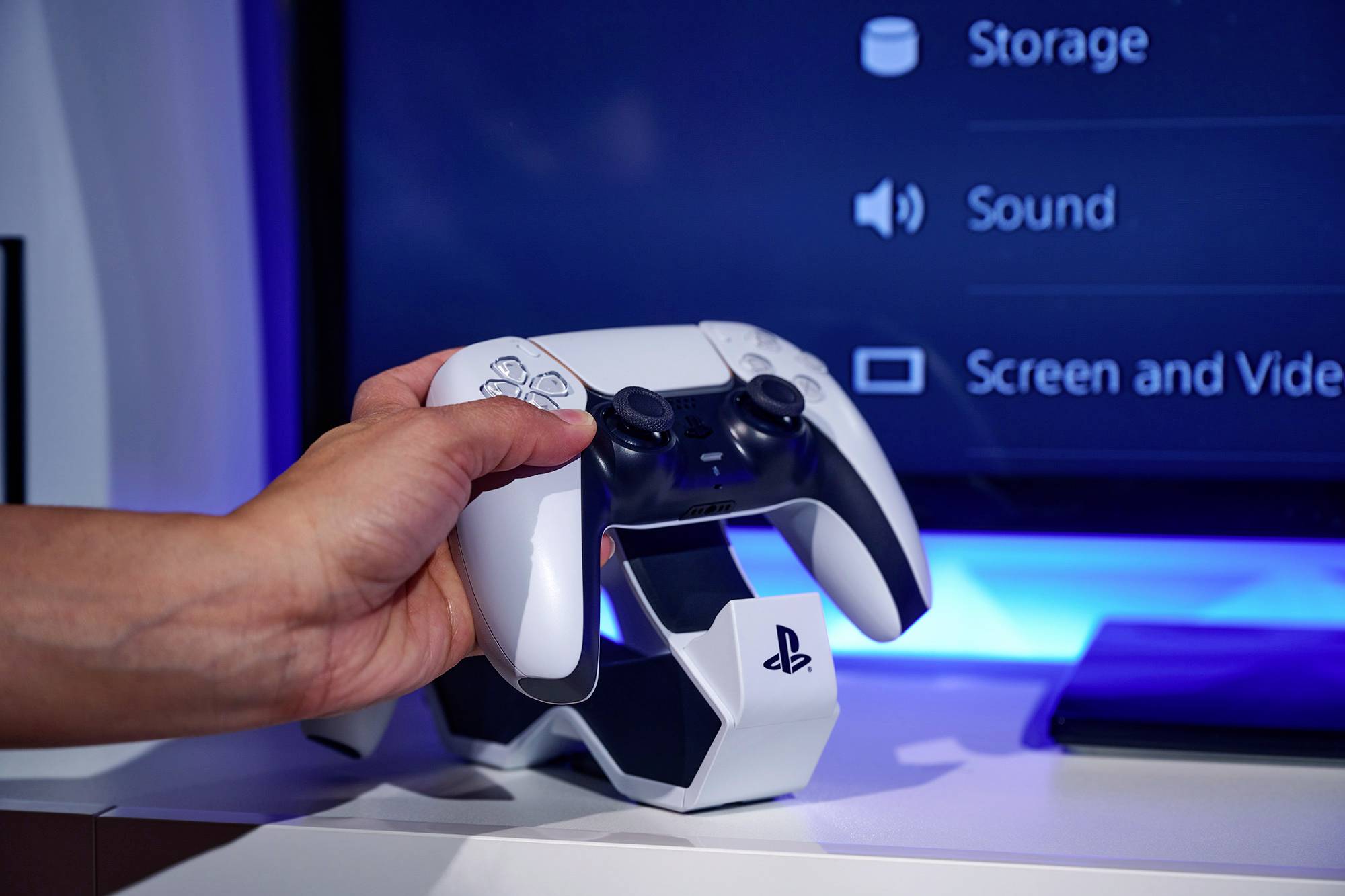 Una mano tiene un controller da gaming bianco davanti a uno schermo che mostra le impostazioni per 'Memoria', 'Audio' e 'Schermo e Video'.