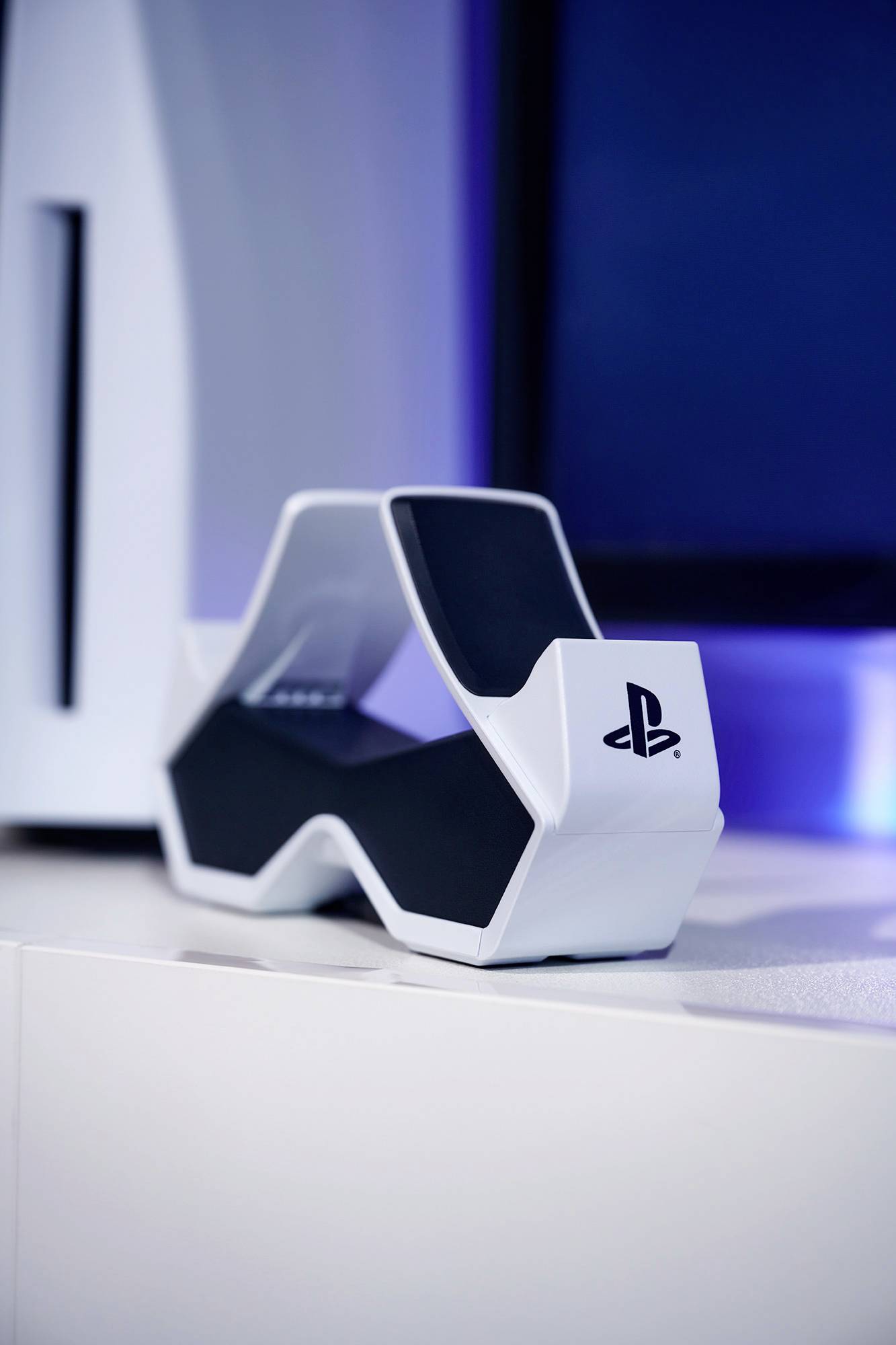 Una stazione per controller PlayStation bianca su uno sfondo blu, con una parte della console visibile a sinistra dell'immagine.