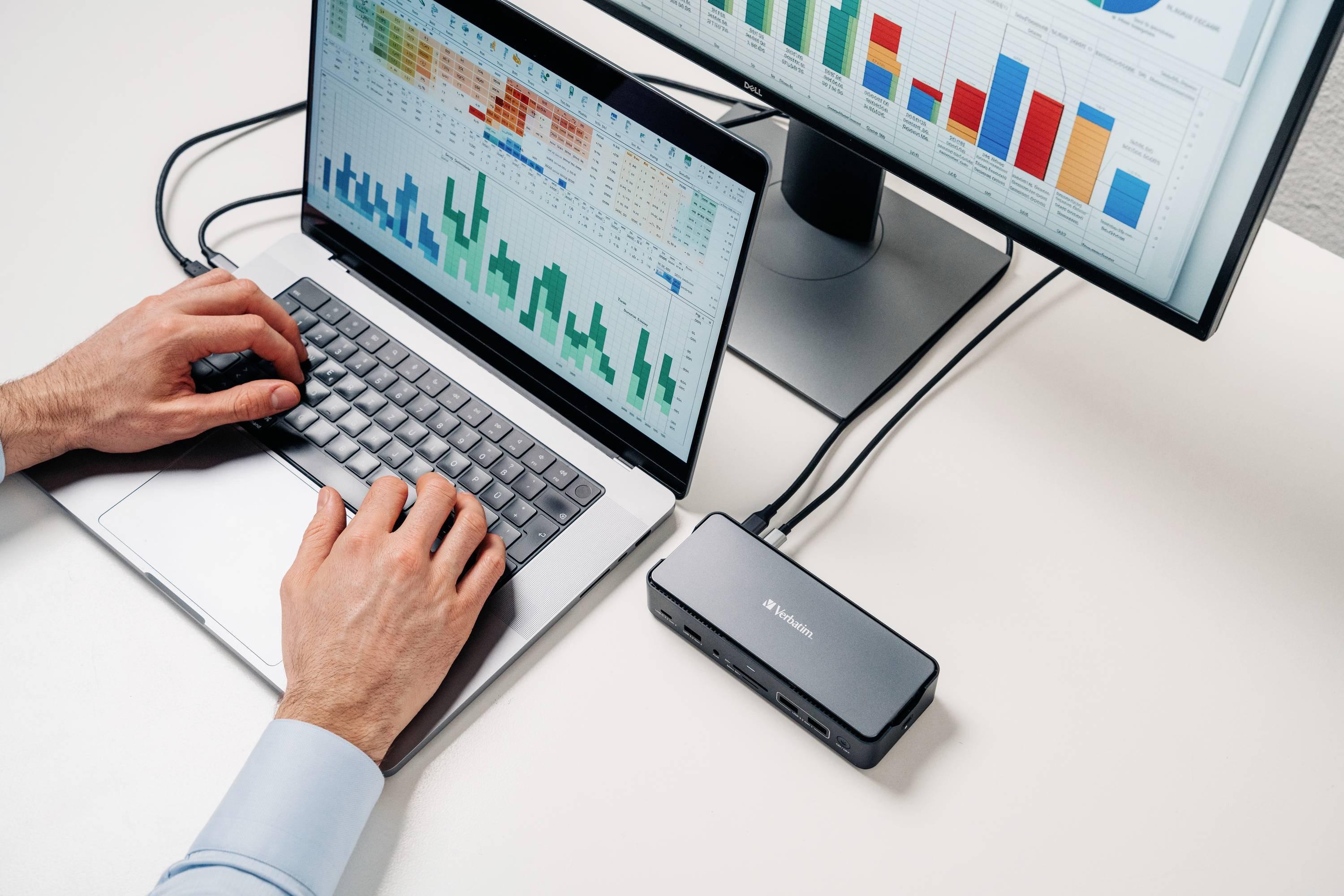 Una persona lavora al laptop, collegato a un monitor che mostra tabelle con diagrammi e grafici a barre.