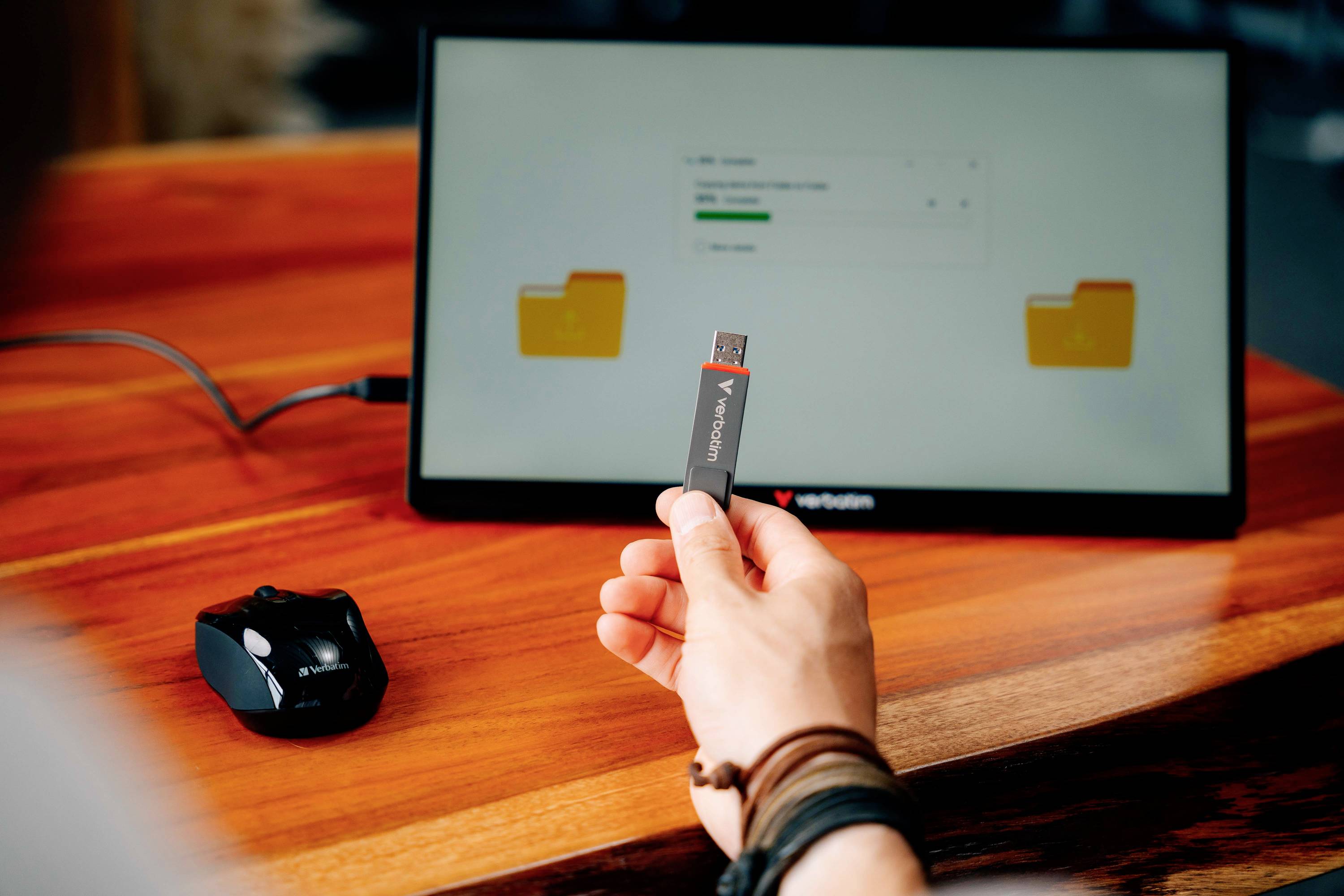 Una persona tiene un'unità USB davanti a uno schermo del computer. Sullo schermo sono visibili due icone di cartelle.