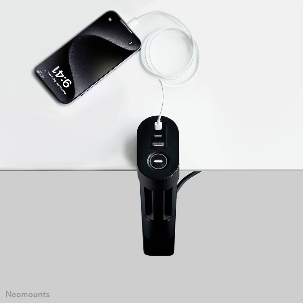 Un smartphone viene collegato a una stazione di ricarica integrata in un tavolo tramite un cavo USB.
