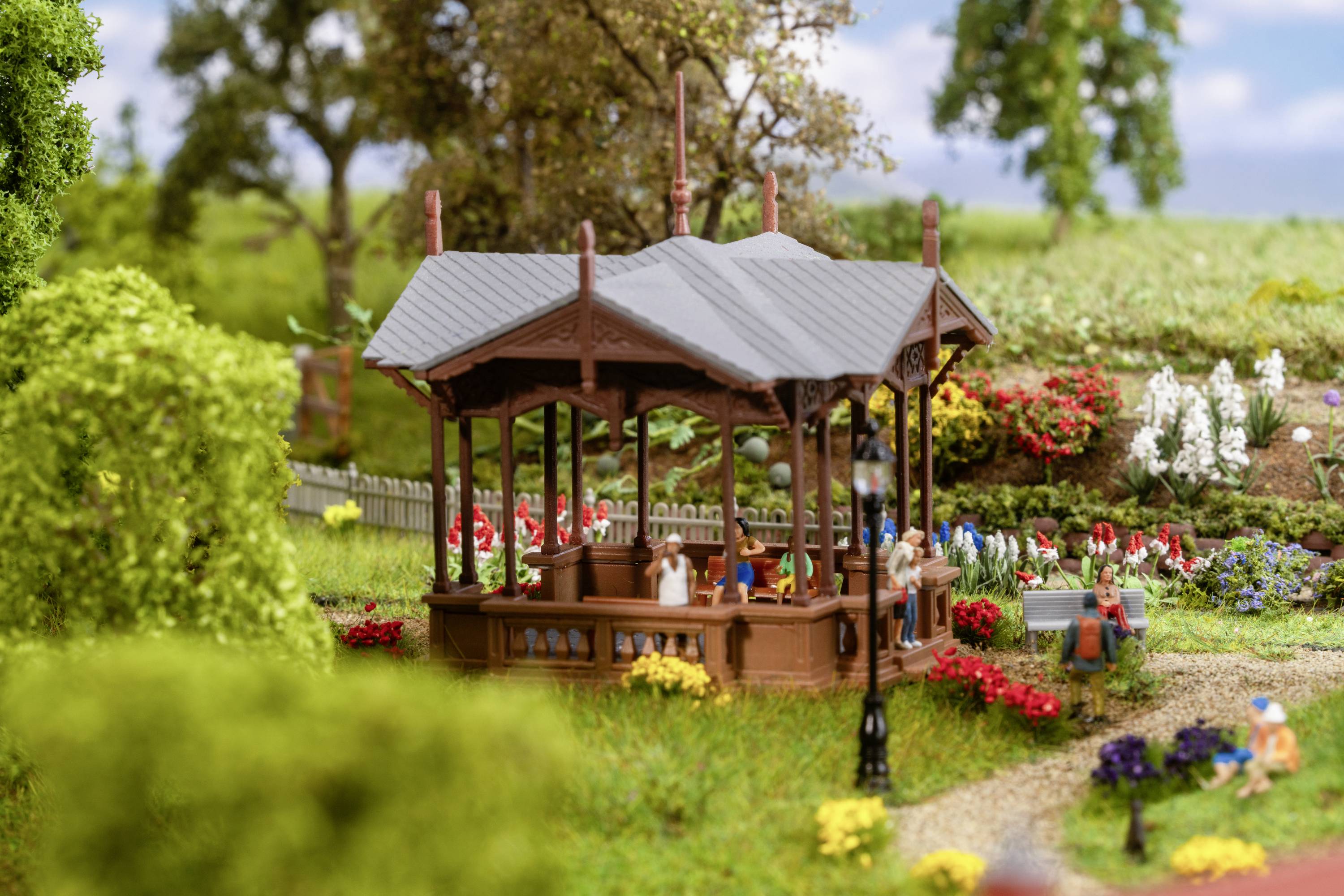 Un modello di parco con un padiglione al centro, circondato da alberi, fiori e figure in miniatura che siedono rilassate nel parco.
