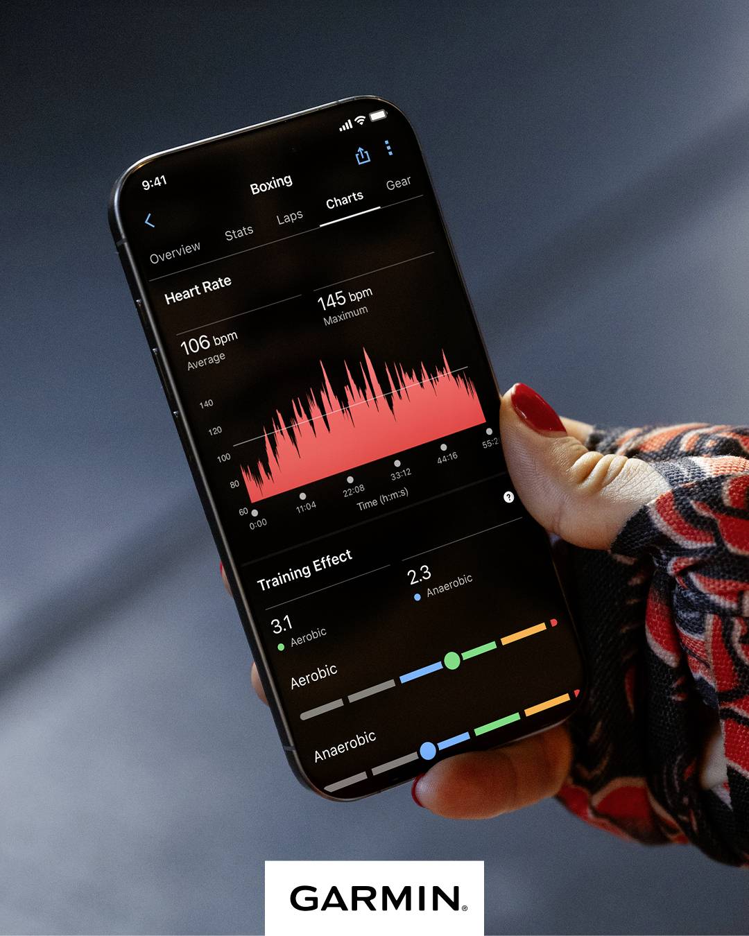Una mano tiene uno smartphone con un'app fitness aperta. L'app mostra i dati della frequenza cardiaca e gli effetti dell'allenamento. In basso c'è scritto 'Garmin'.