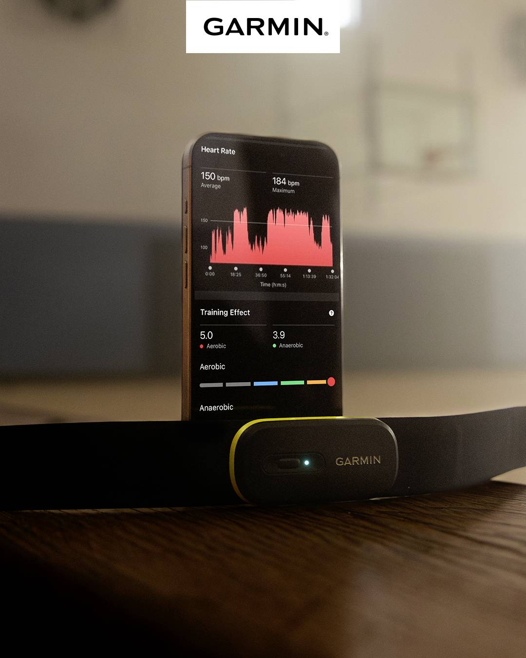 Sensore 'Garmin' davanti a smartphone con visualizzazione di frequenza cardiaca e dati di allenamento in palestra.