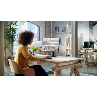 Una persona seduta in un ufficio luminoso è seduta a una scrivania, guardando uno schermo del computer che mostra un sito web di un'agenzia di viaggi con varie immagini di destinazioni.