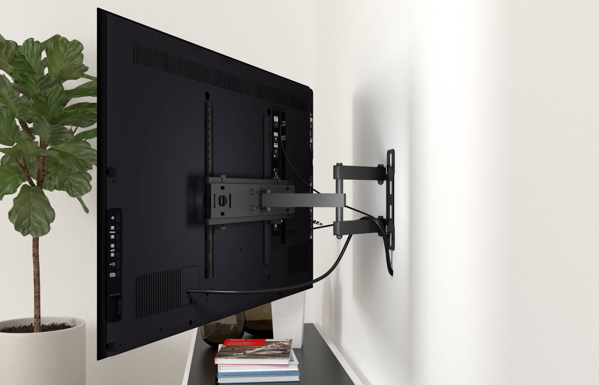 Televisore a schermo piatto montato a parete su un braccio regolabile accanto a una pianta in vaso, con libri impilati sullo scaffale sottostante.