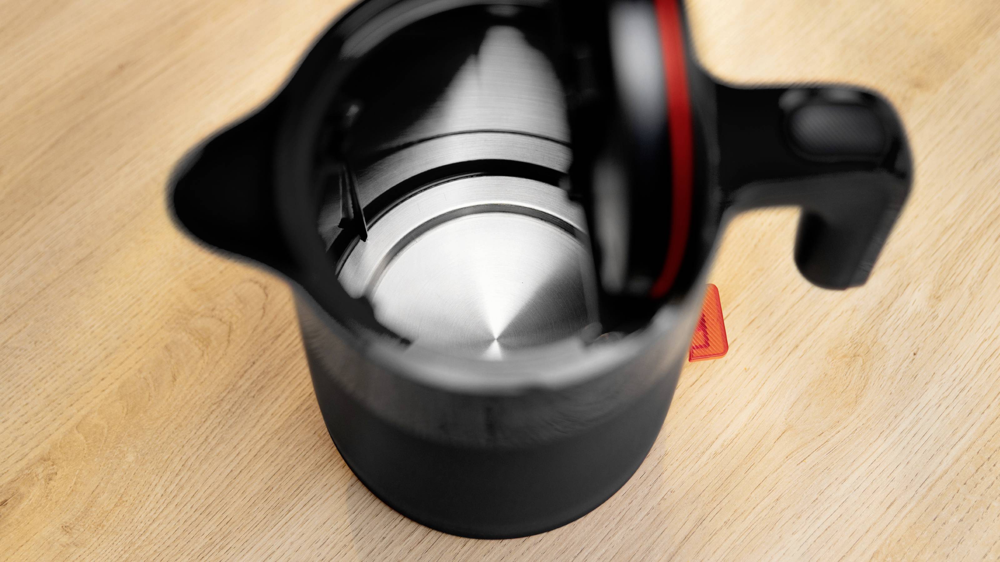 Un bollitore elettrico nero con il coperchio aperto è posizionato su una superficie di legno, che mostra il suo interno metallico lucido.