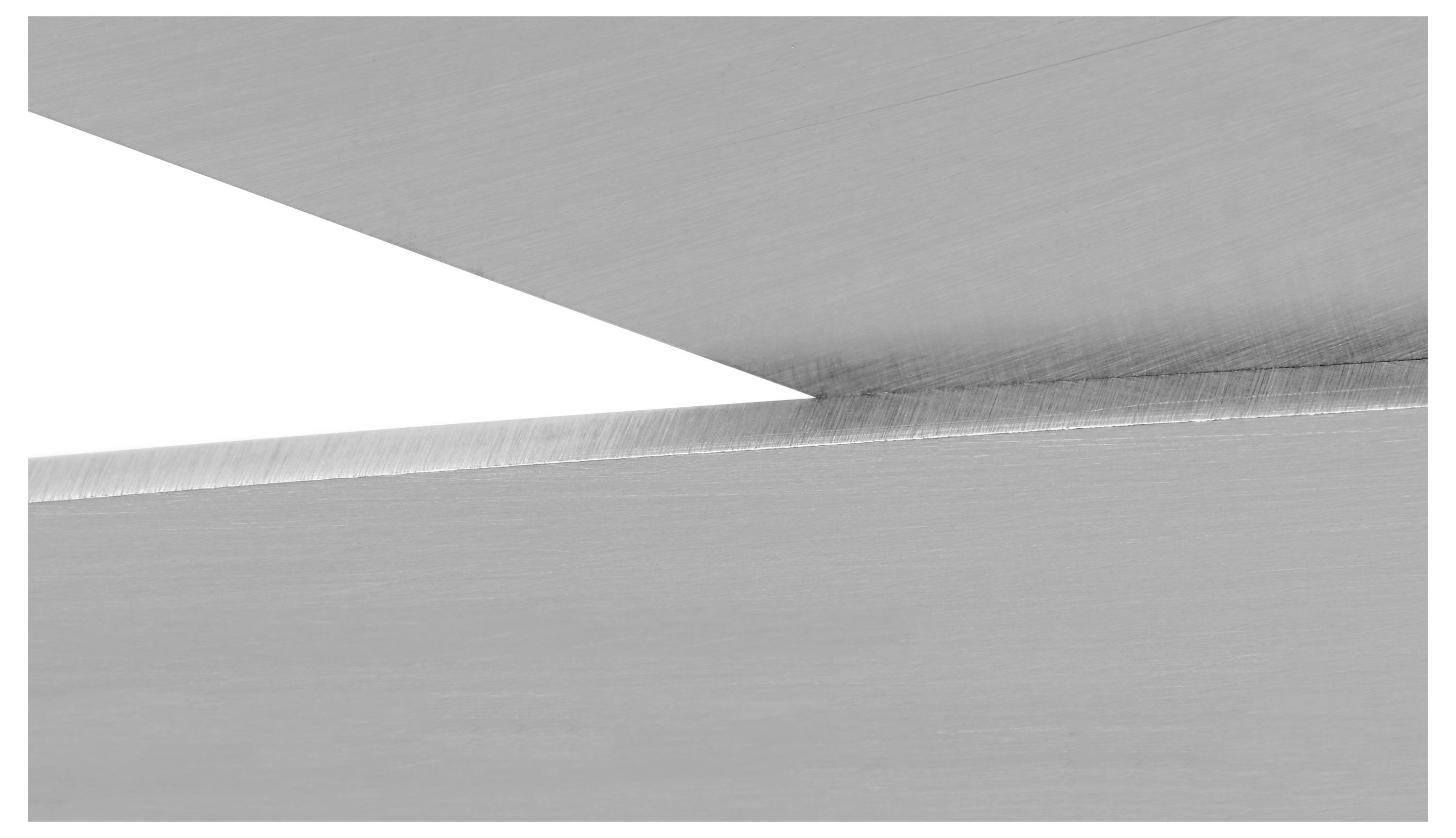 Primo piano di due superfici metalliche che si intersecano, creando una linea nitida e angolare tra loro, che evidenzia la texture e la precisione.