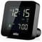 Un orologio digitale che mostra '12:15' con una sveglia impostata alle '7:00'. Lo schermo indica inoltre l'ora legale (DST) e un simbolo di campanello della sveglia.
