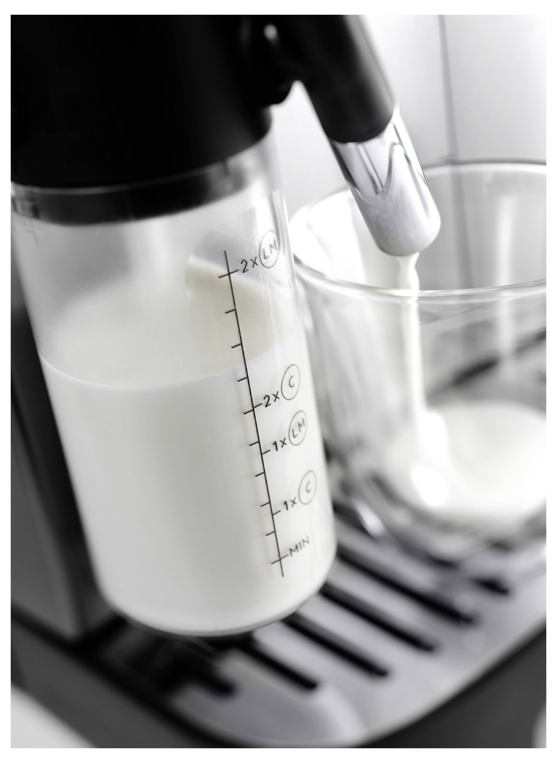 'Un montalatte sta montando attivamente il latte in un bicchiere trasparente posizionato su un vassoio, con i segni di misurazione visibili sul contenitore del montalatte.'