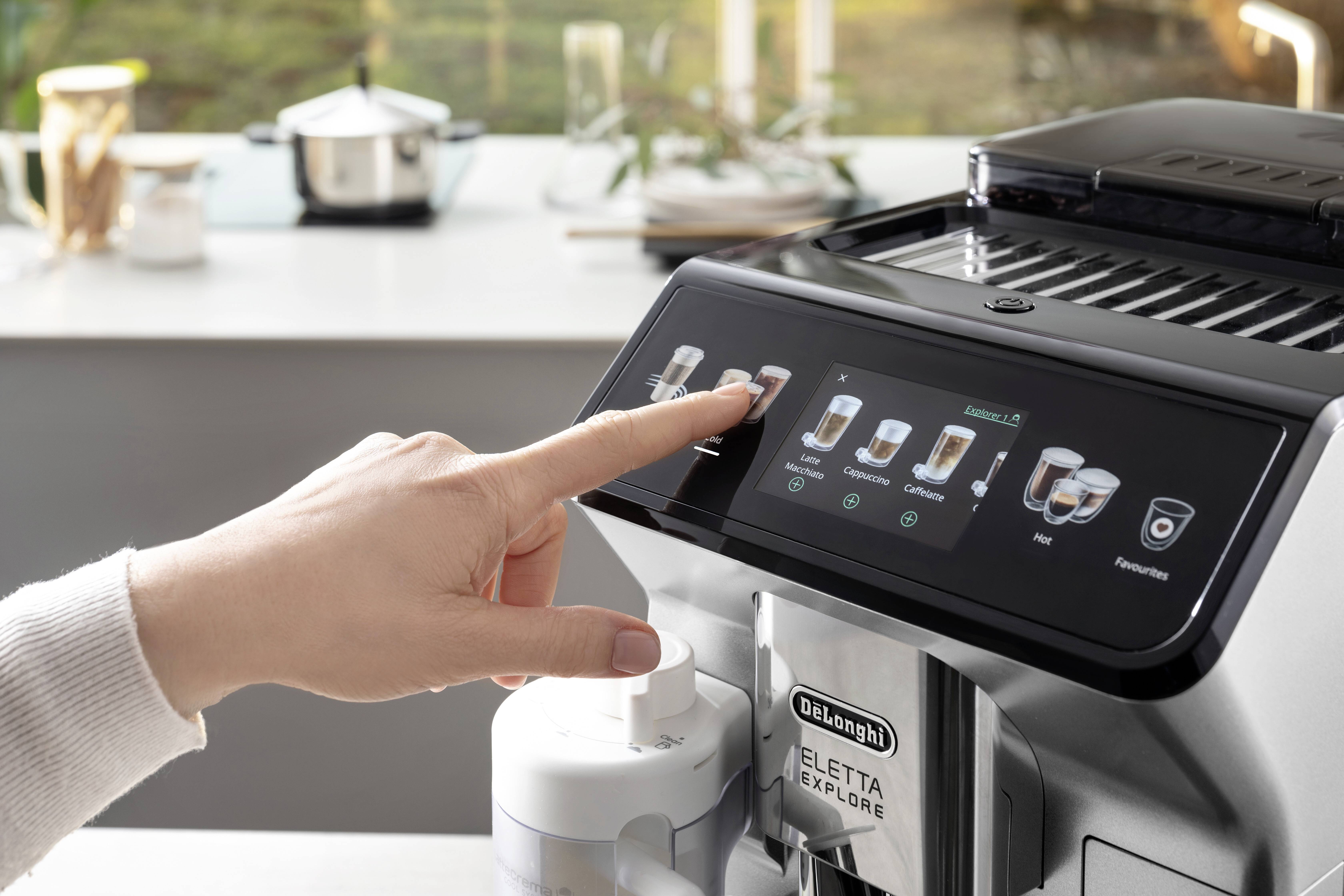 Una mano seleziona un'opzione di bevanda sul touchscreen di una macchina da caffè De'Longhi Eletta Explore in un ambiente cucina moderno.