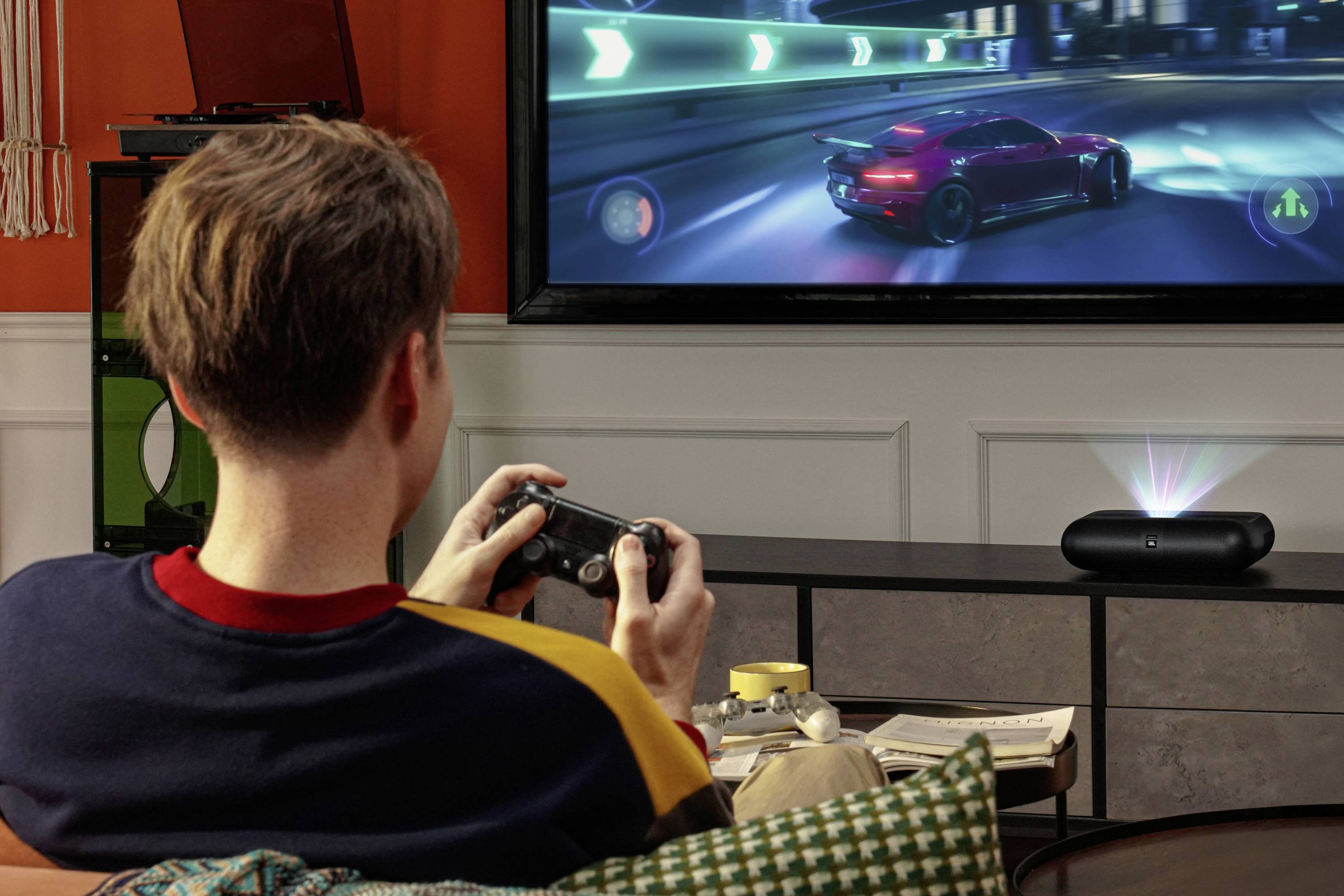 Una persona sta giocando a un videogioco di corse su un grande schermo, utilizzando un controller. Un'auto sta gareggiando su una pista luminosa e vibrante.