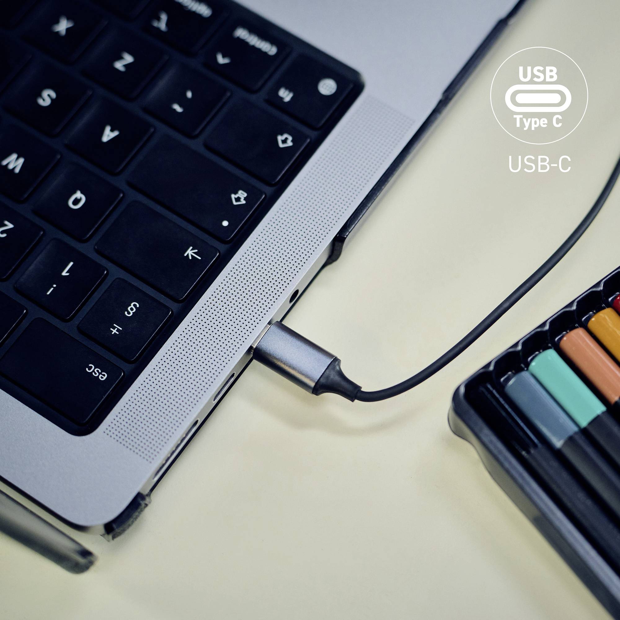 Un cavo USB Type-C è collegato a un laptop, circondato da pennarelli colorati su una scrivania, che evidenzia la versatilità delle porte USB-C.
