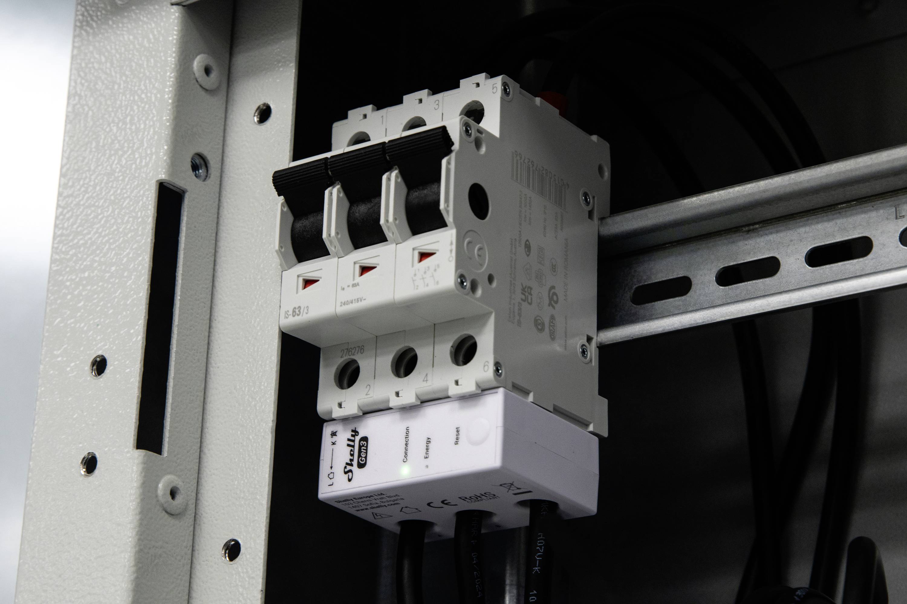 Un primo piano di un quadro elettrico con tre interruttori in posizione di accensione. Il pannello è montato all'interno di un armadio metallico.